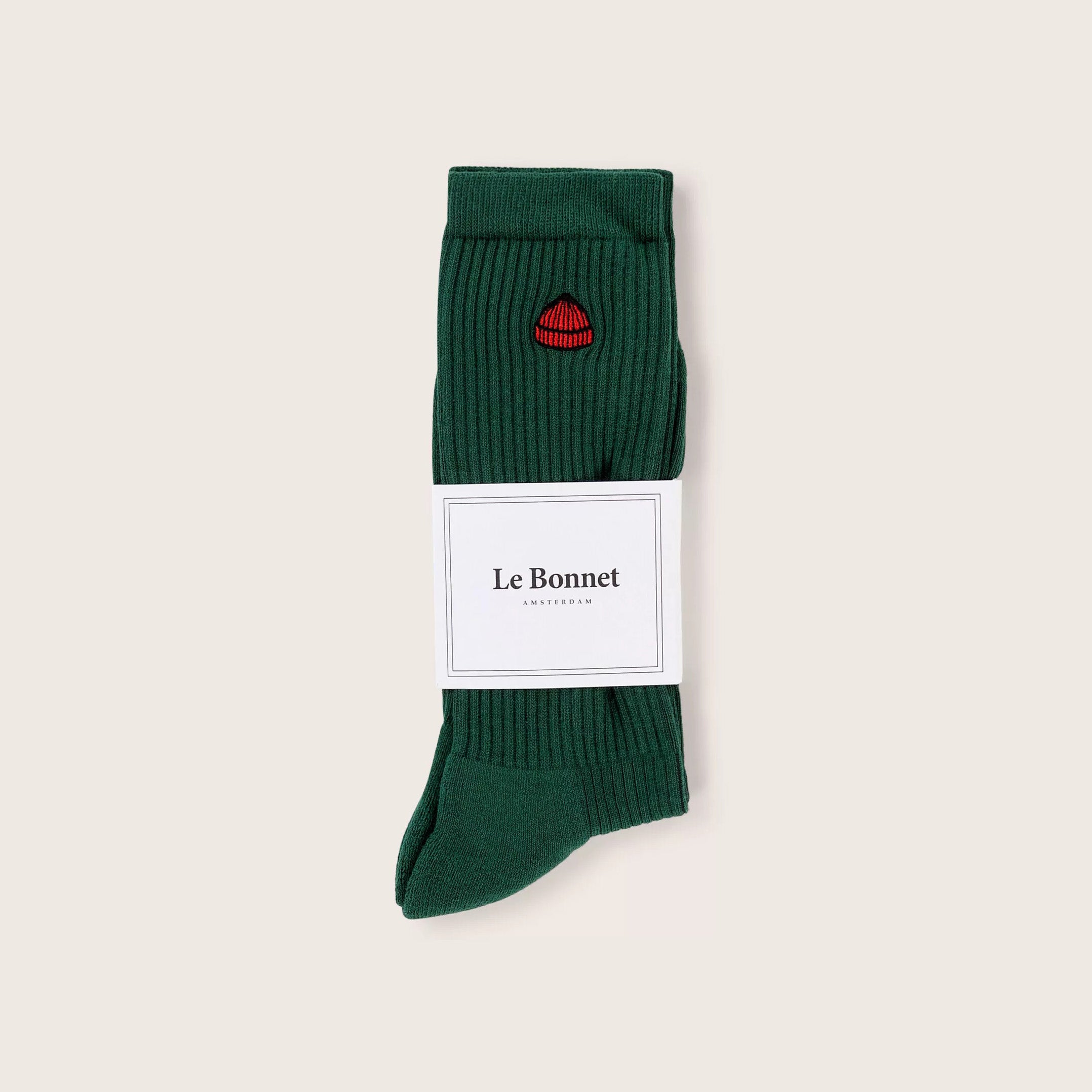A pair of folded green ribbed Tube Sock, Pine by Le Bonnet, made from a soft cotton blend with a small red lips design, wrapped in a white "Le Bonnet" label on a light background.