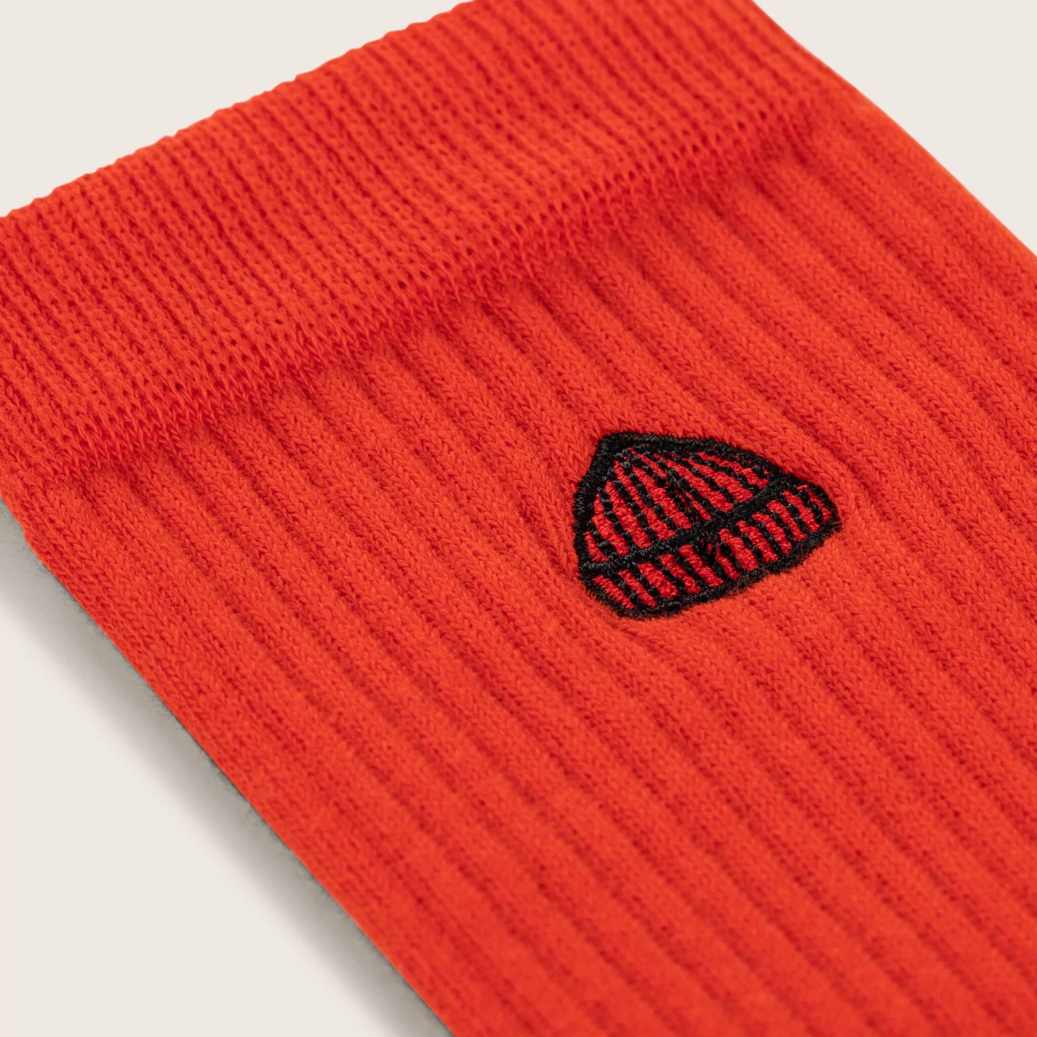 Close-up of the Le Bonnet Tube Sock in Crimson, made from a ribbed cotton blend and featuring a small black and white Beanie signature hat embroidery.