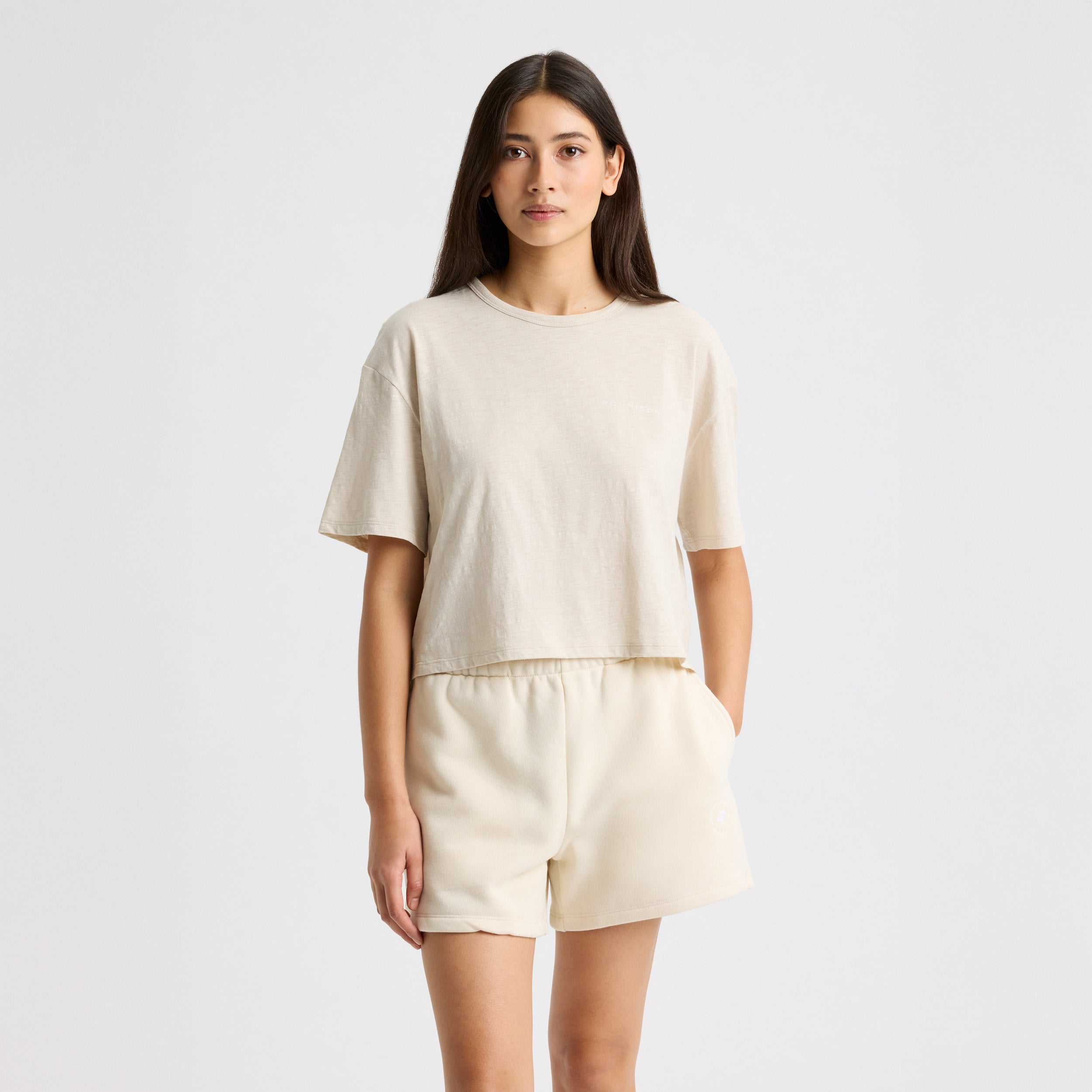 Against a plain backdrop, someone dons Rohnisch's beige Slub Cropped Tee and matching shorts. The tee's boxy fit accentuates the casual elegance of in-conversion cotton, crafting a relaxed yet stylish look.