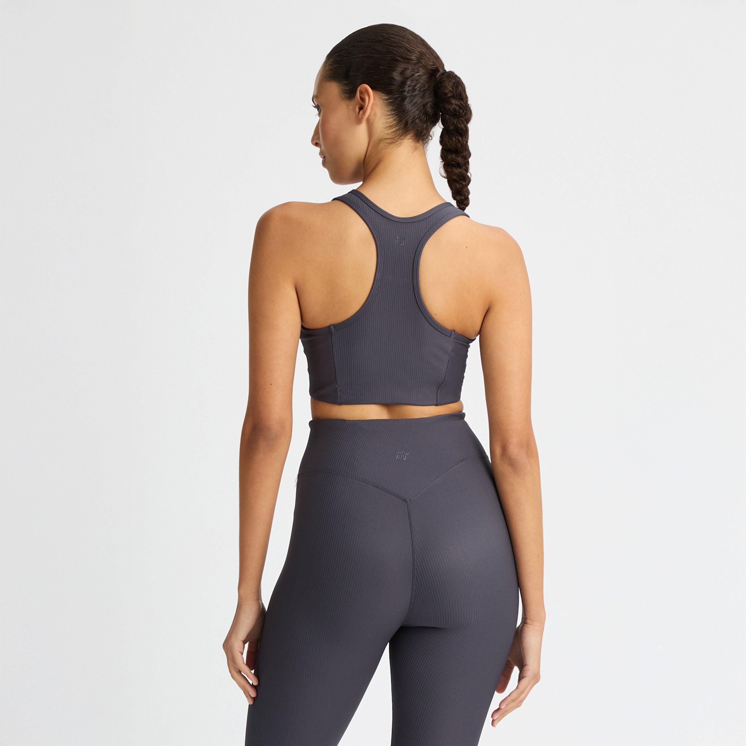 A person models a dark gray Rohnisch athletic outfit with a medium-support Ribbed Sportsbra and matching recycled polyester leggings, standing with their back turned.