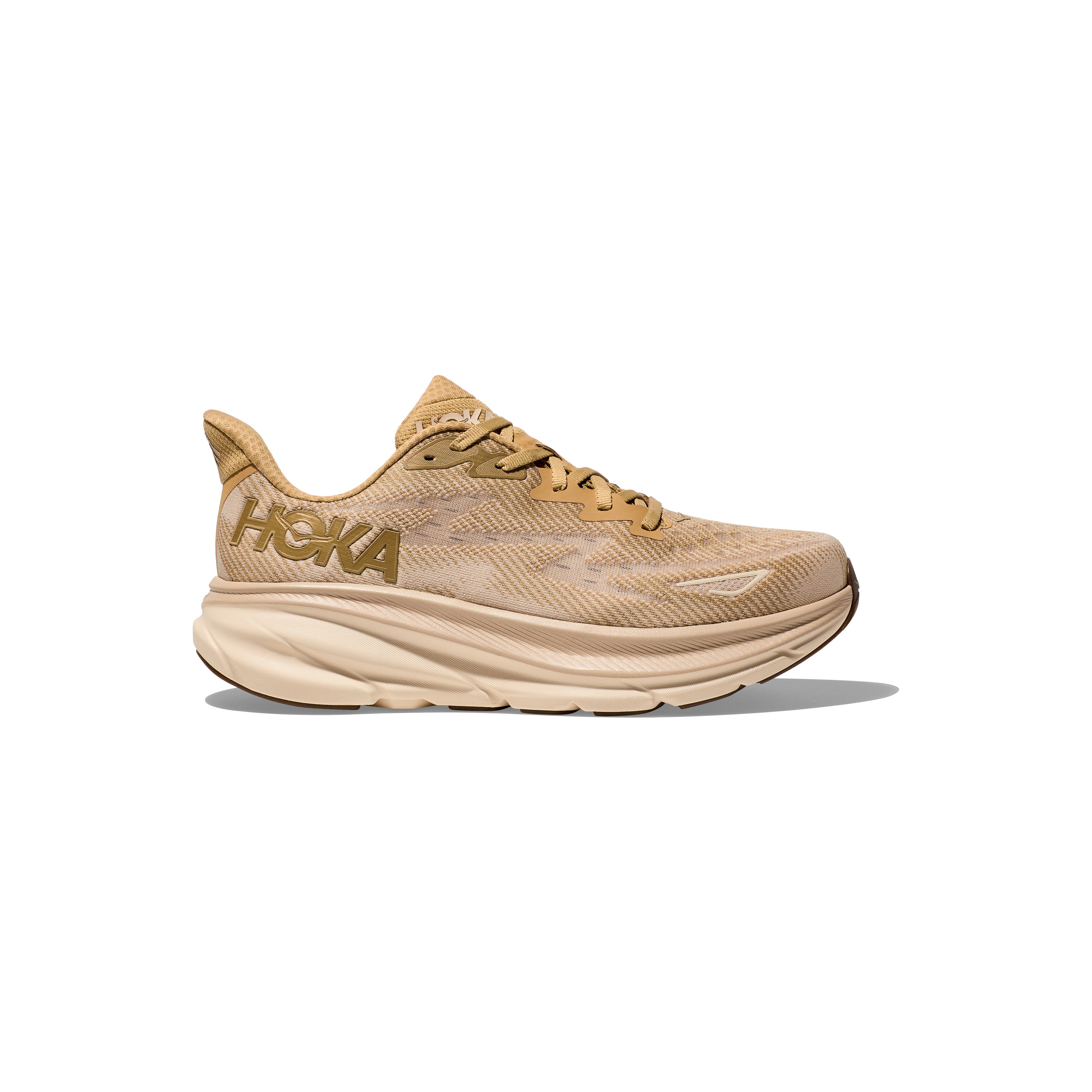 The Hoka M Clifton 9 in Wheat/Shifting Sand features a thick, cushioned sole and mesh upper. Shown side view on white background, this shoe provides responsive toe-off with every stride.