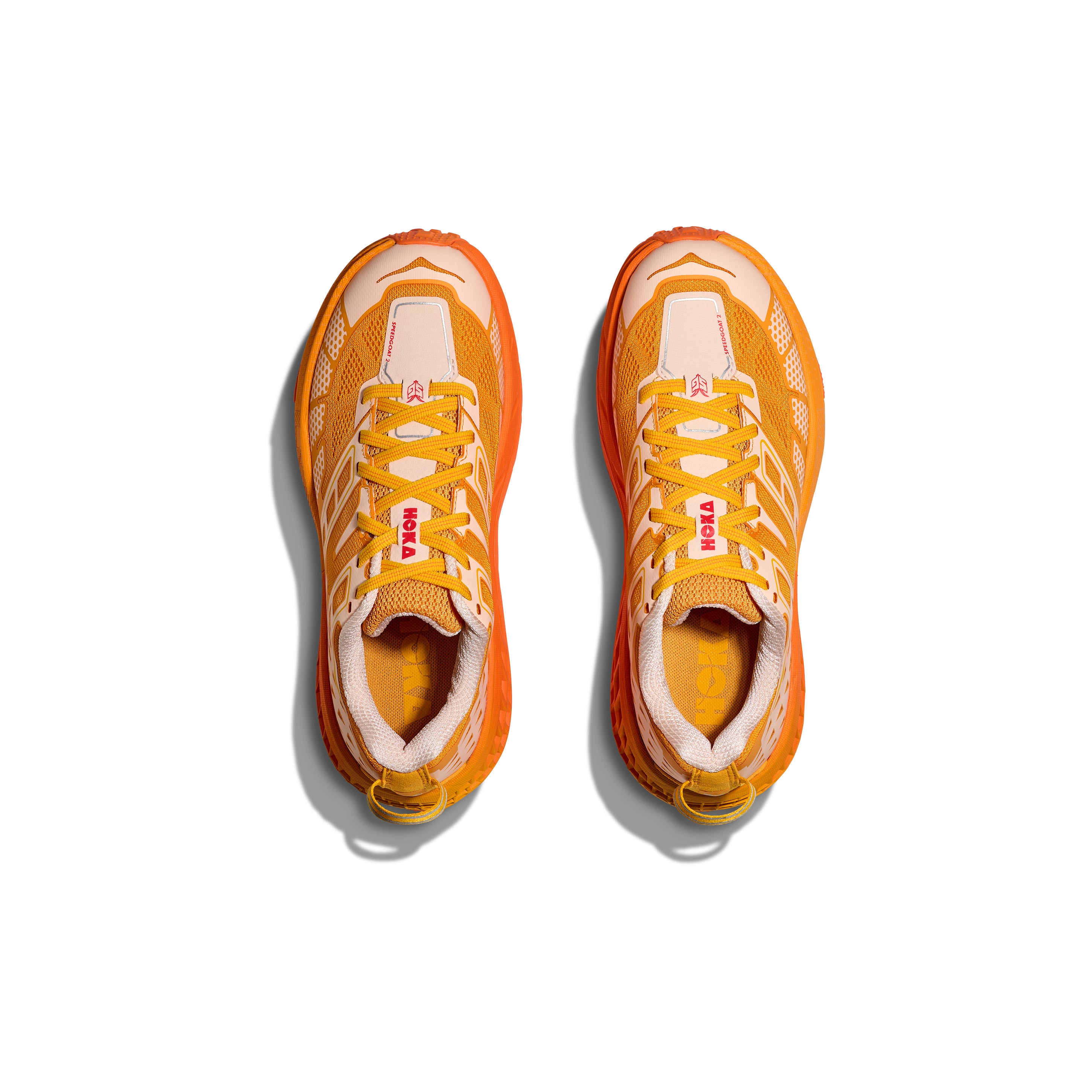 A top-down view of the Hoka U Speedgoat 2 sneakers in orange and white, featuring mesh uppers, Vibram lugs, and prominent "HOKA" branding, displayed against a white background.