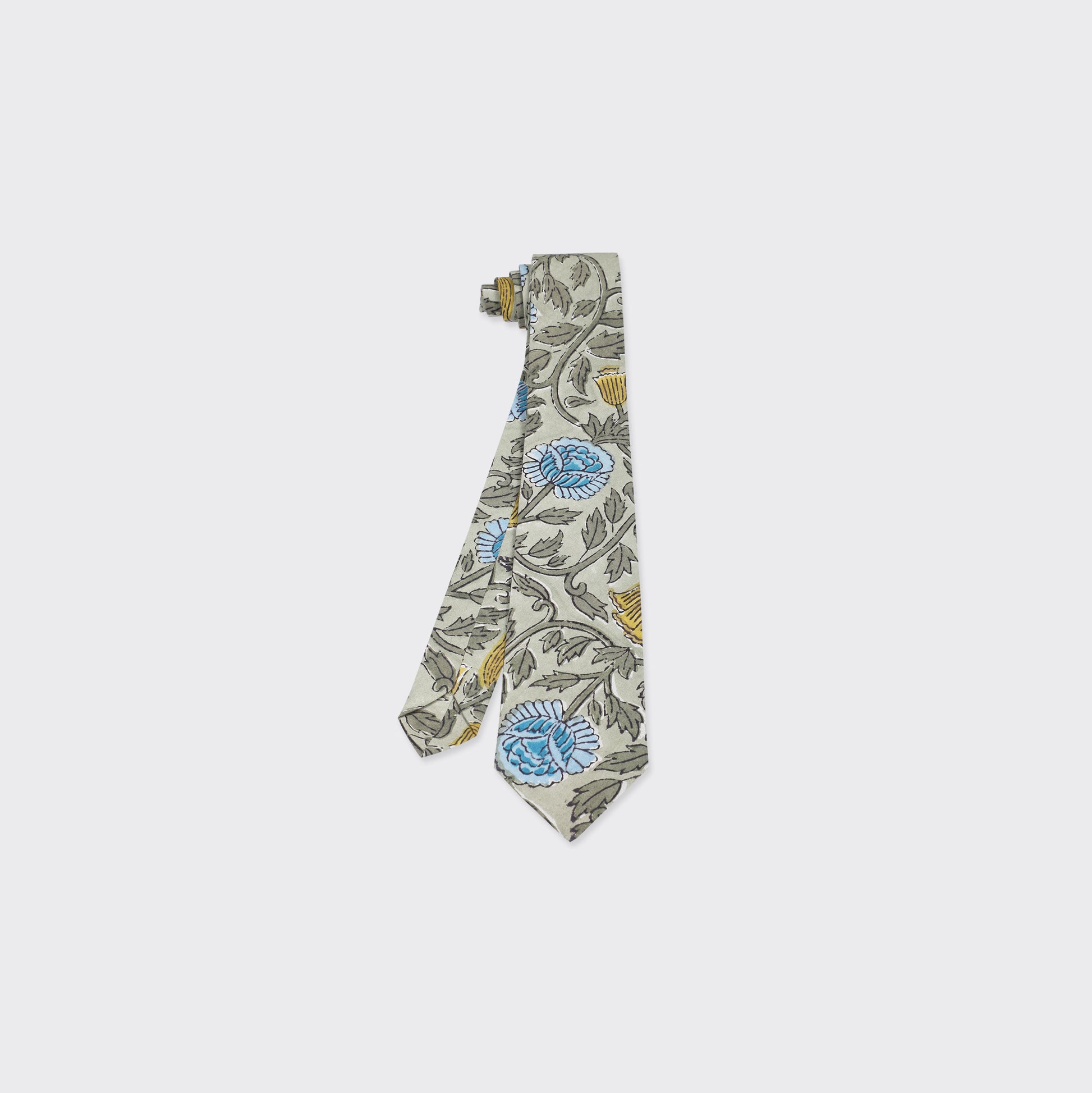 The Kardo Tie, Block Print 137, is a light beige necktie with blue and yellow floral patterns and green leaves, shown on a plain white background.