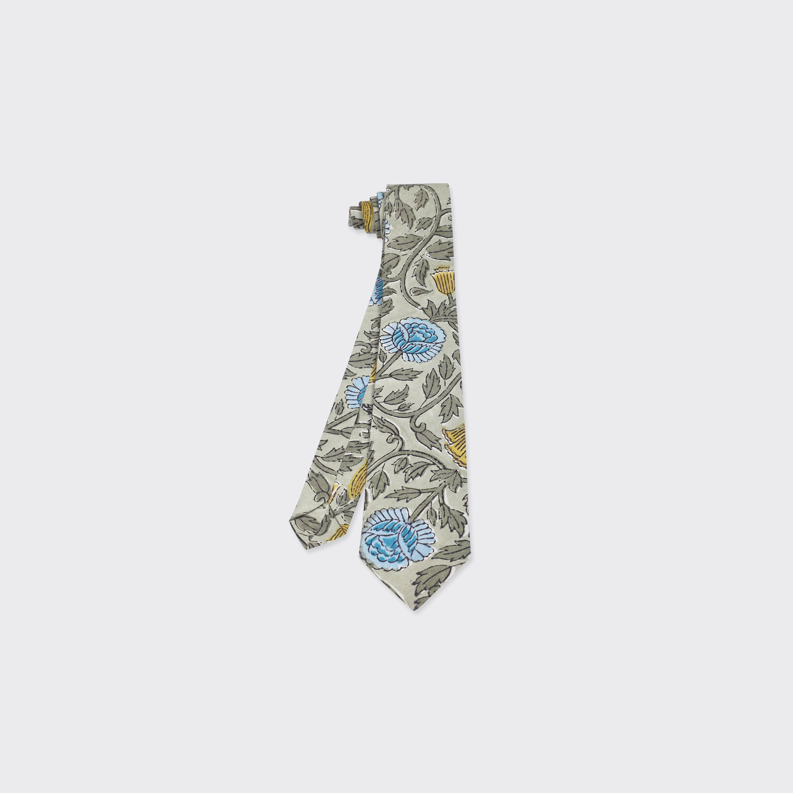 The Kardo Tie, Block Print 137, is a light beige necktie with blue and yellow floral patterns and green leaves, shown on a plain white background.
