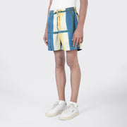 Person wearing a white top, Kardo Olbia Shorts in Yellow Clamp Dye, and white sneakers, standing against a plain light background.
