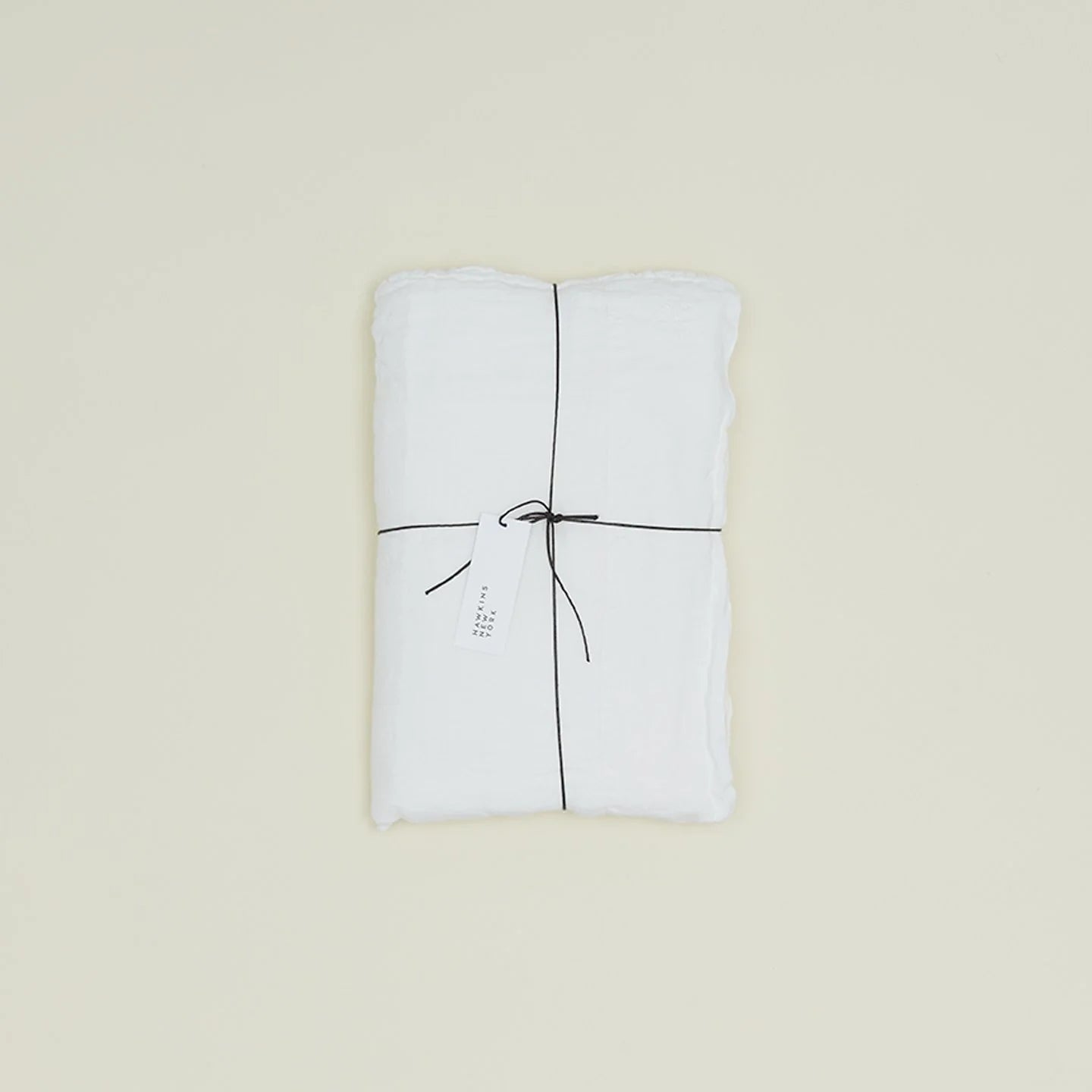 A neatly folded Hawkins New York Simple Linen Bedding - Queen Flat Sheet in white, tied with black string and a white tag, rests on a plain light background. Woven in Portugal for timeless quality.