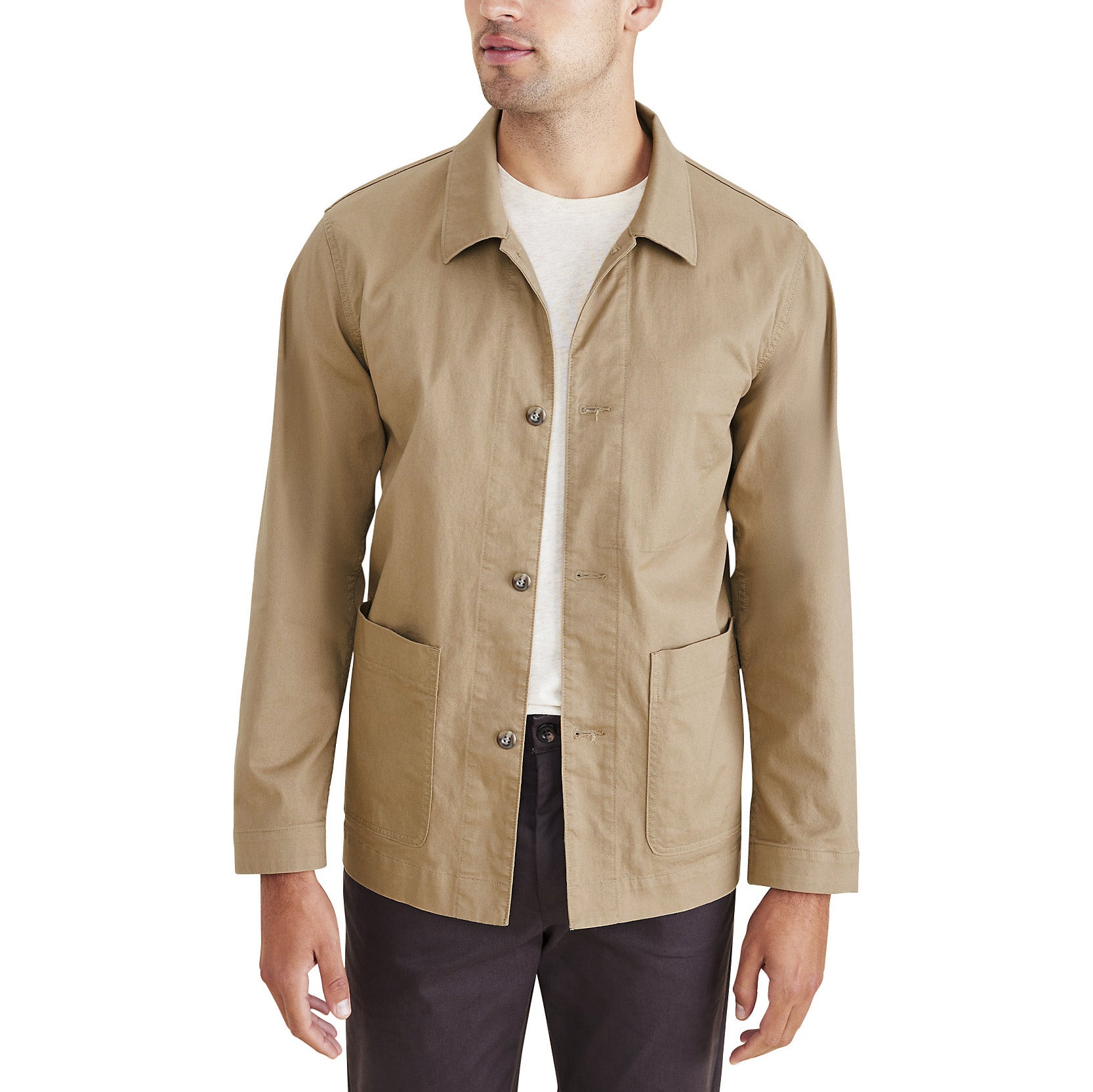 A man dons a Dockers Men's Chore Coat in beige, crafted from recycled nylon for stretch comfort. It’s worn over a white shirt and dark pants, featuring two large front pockets.