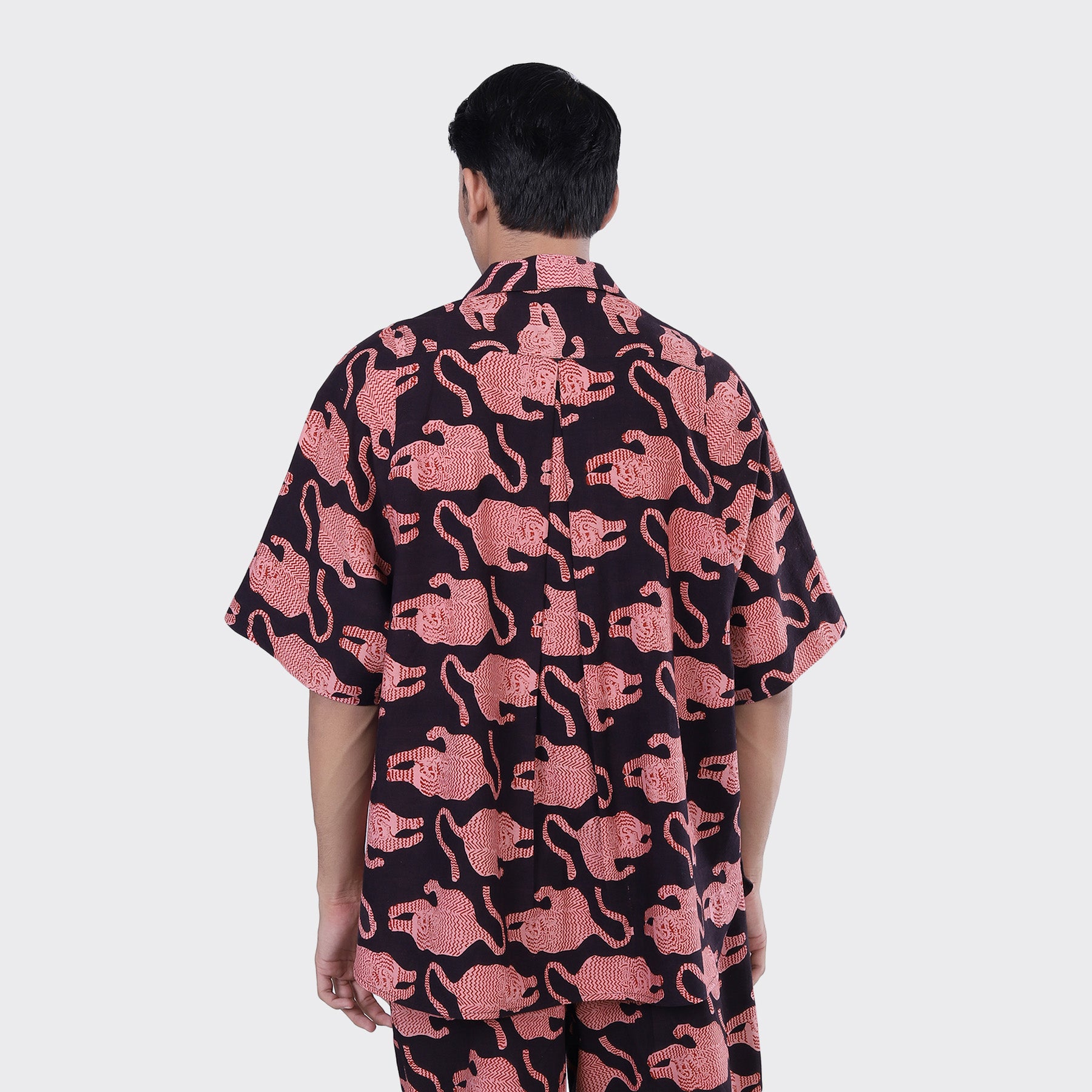 A person stands facing away, wearing the Kardo Yusuke Shirt in Coral Block Print, a short-sleeve button-up with an abstract pink and black design, set against a plain light background.