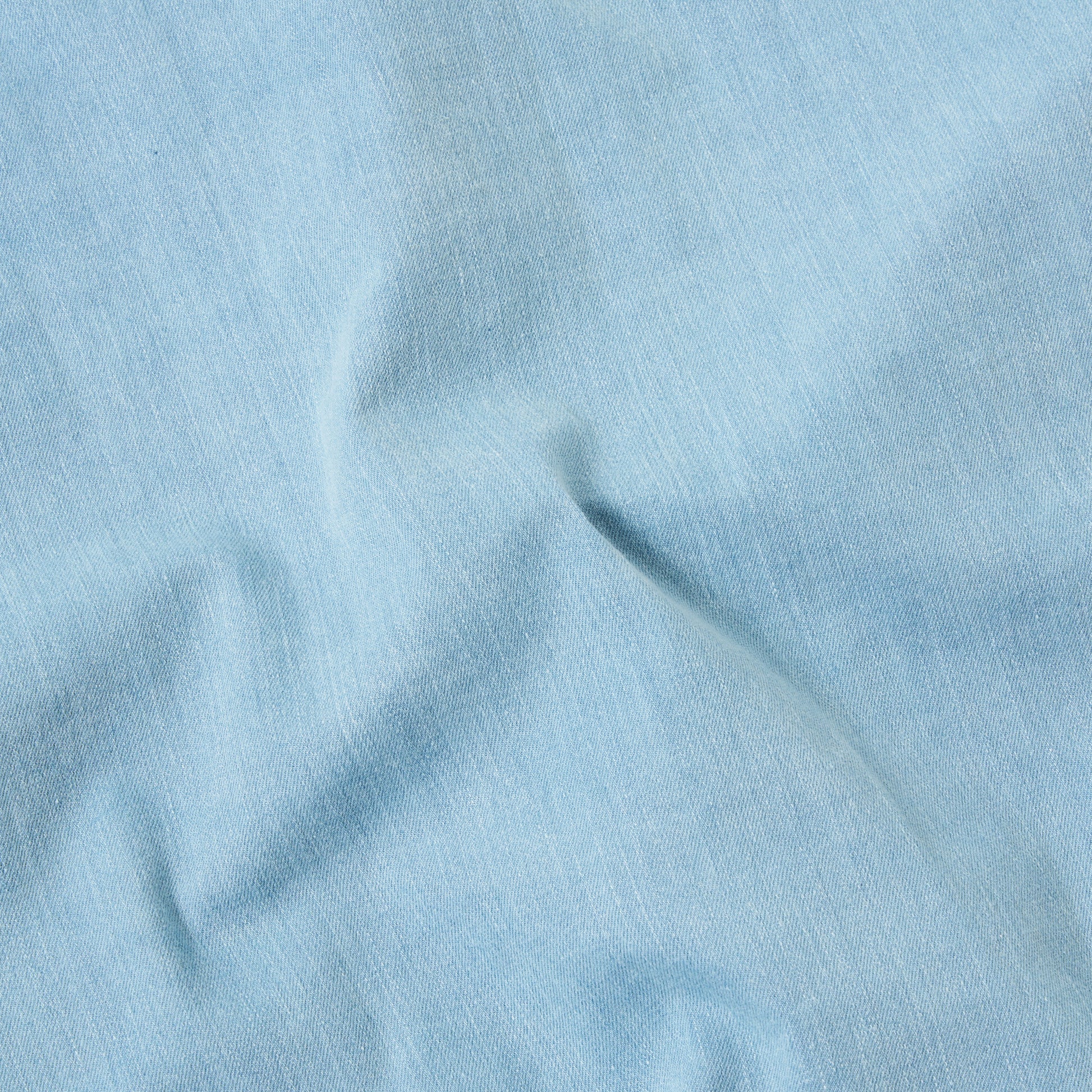 Close-up of the 8 Oz Organic Denim Dockside Jacket in Washed Indigo by Universal Works, highlighting its light blue color with visible creases and texture.