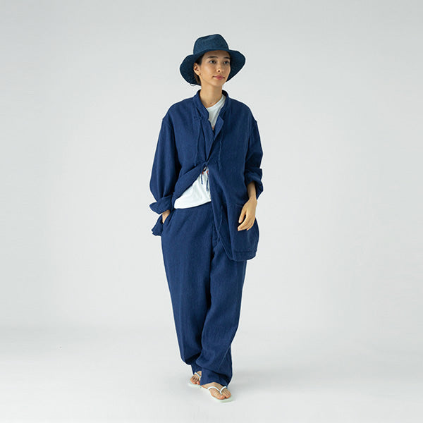 A person wears the Sublime Roe Paper Croquet Mountain Hat with a loose blue jacket and matching pants over a white shirt, standing against a plain, light background.