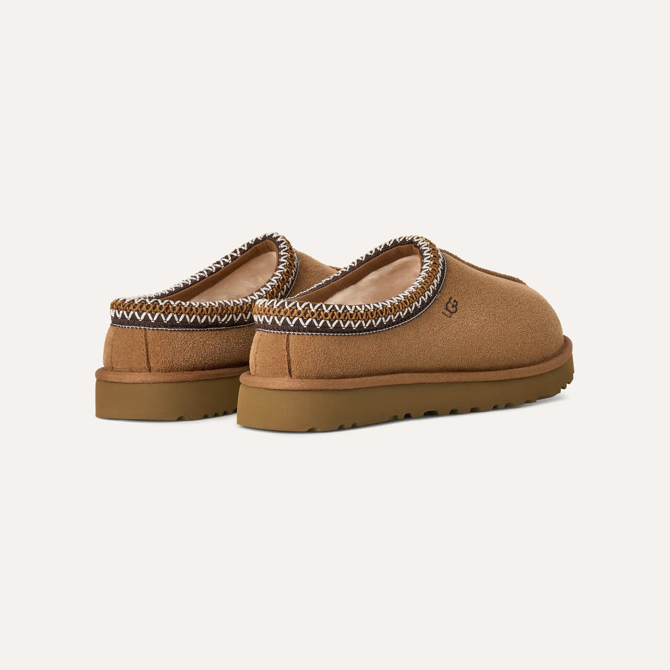 The Ugg W's Tasman features tan suede slip-on shoes with a zigzag stitch around the opening and an ultra-lightweight rubber sole, shown from the rear.