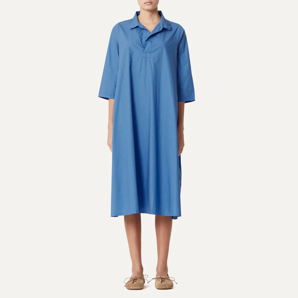 A person wearing the Labo Art Abito Pepe Dress, Clara stands against a plain background. The dress is a loose-fitting, knee-length blue poplin design with a collar and elbow sleeves.