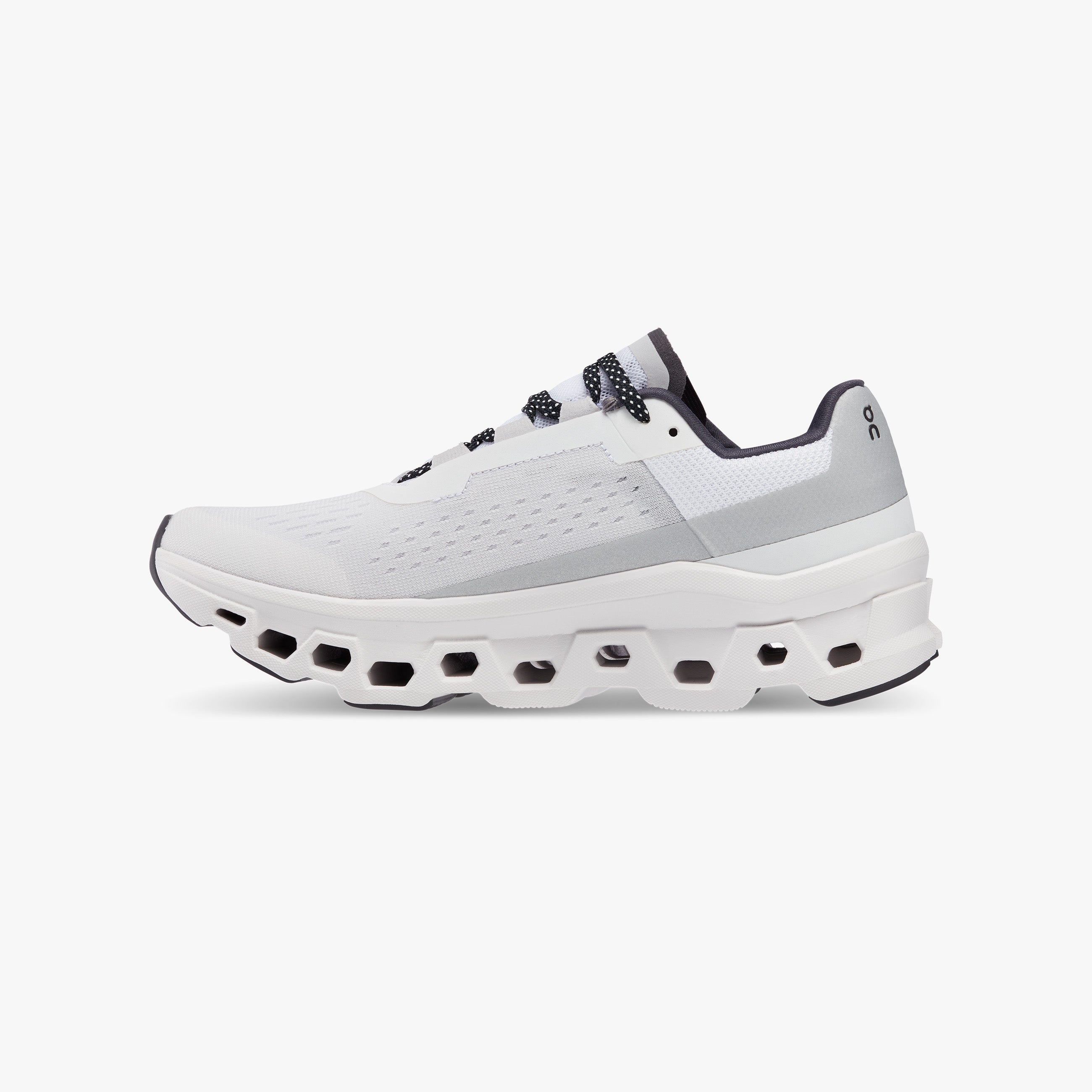 The On Running M Cloudmonster in All White features max cushioning with Helion™ superfoam, a thick sole with hexagonal cutouts, mesh upper, and black and gray accents—shown side profile on a white background.