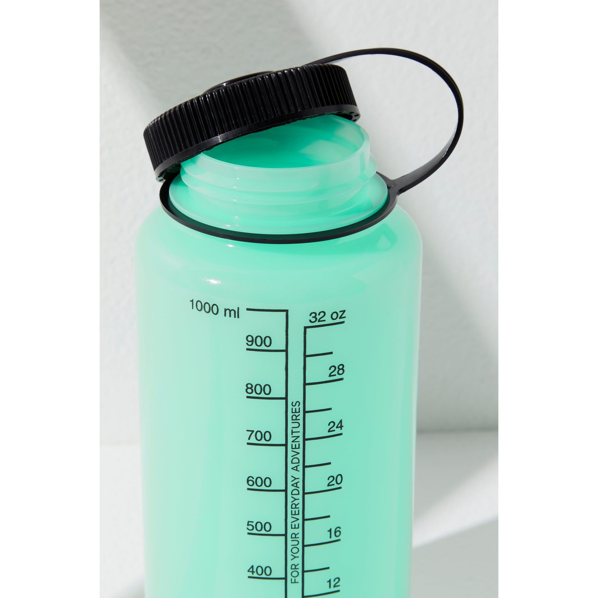 Close-up of a GITD water bottle from Free People Movement with measurement markings and a black lid, highlighted by sunlight.