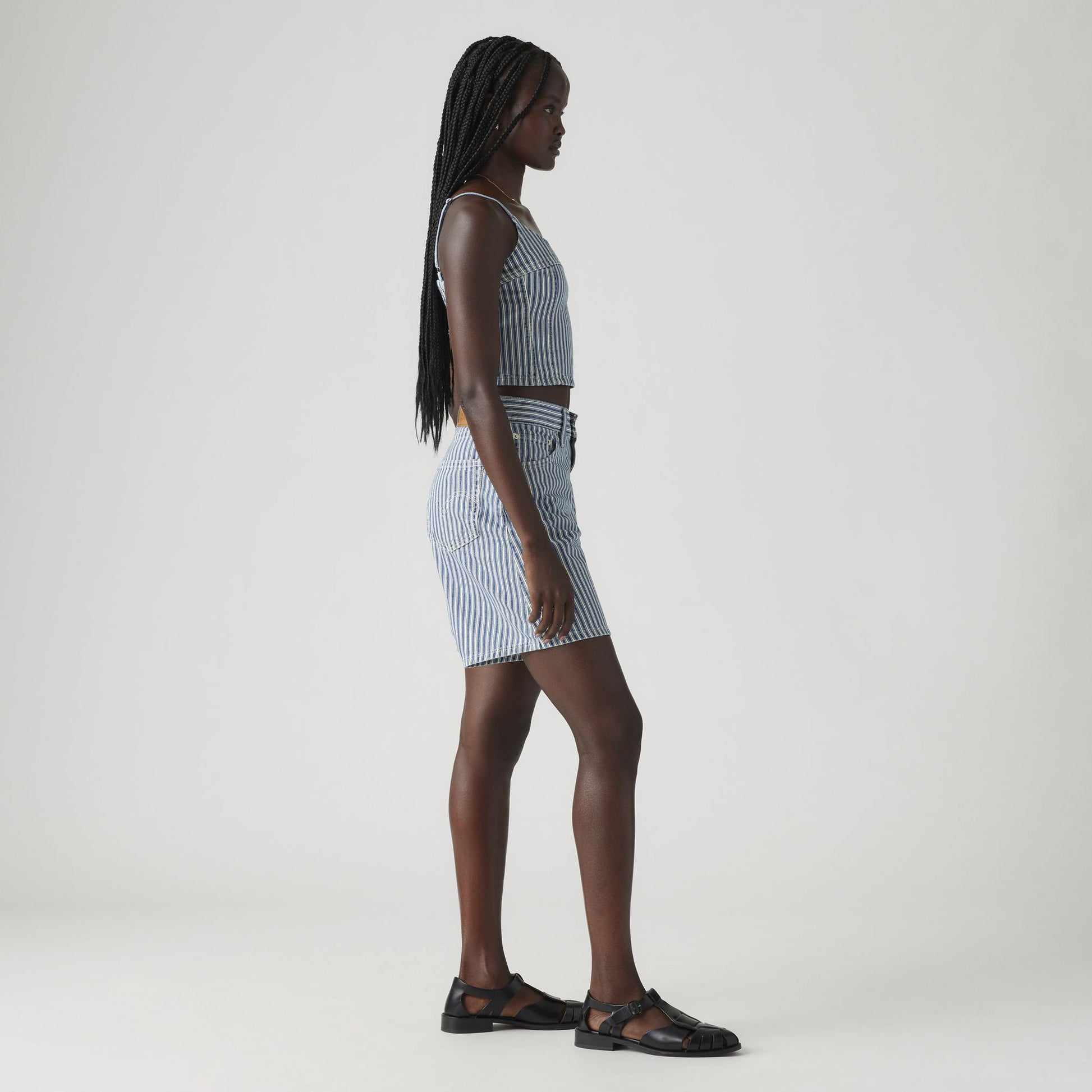 A woman in profile wears Levi's High Baggy Short and a matching vintage-inspired blue and white striped sleeveless crop top with black sandals against a plain light background.