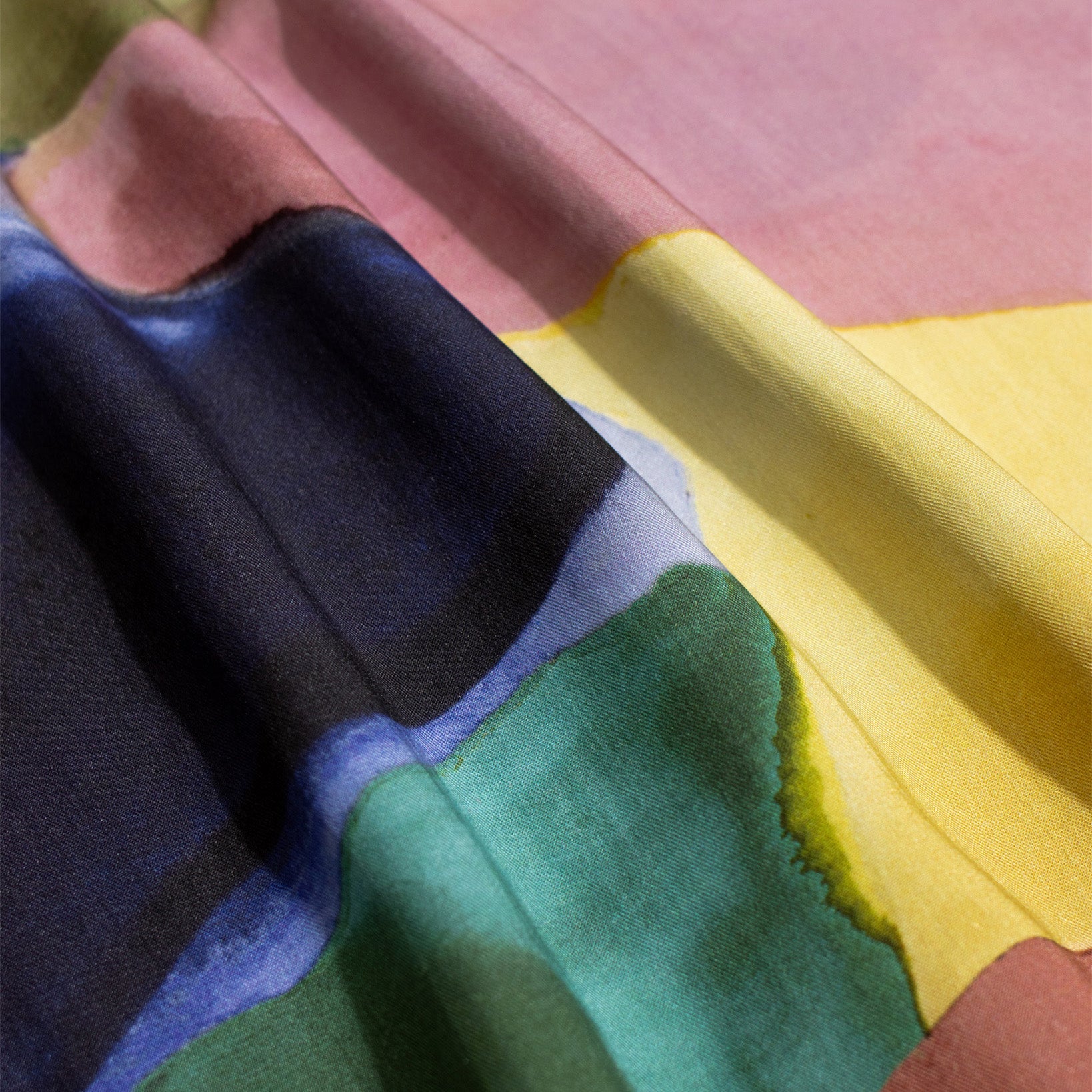 Close-up of the Far Afield Busey SS Shirt, Painted Landscape, showing fabric with abstract shapes in black, blue, green, yellow, and pink; visible folds and shadows highlight the colorful design.