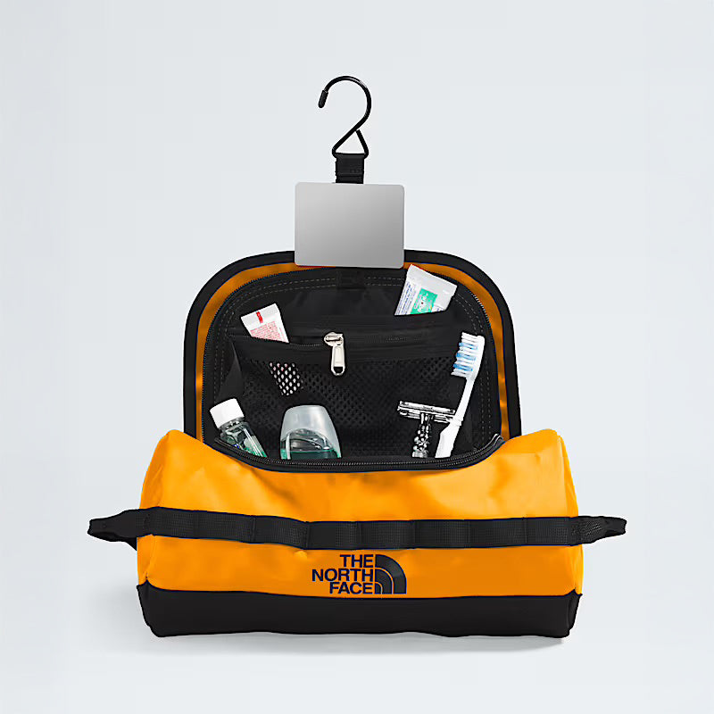 A Summit Gold Base Camp Travel Canister by The North Face hangs open from a hook, neatly organizing toiletries like a toothbrush, razor, deodorant, and travel-sized bottles in mesh pockets inside this durable carry-all.