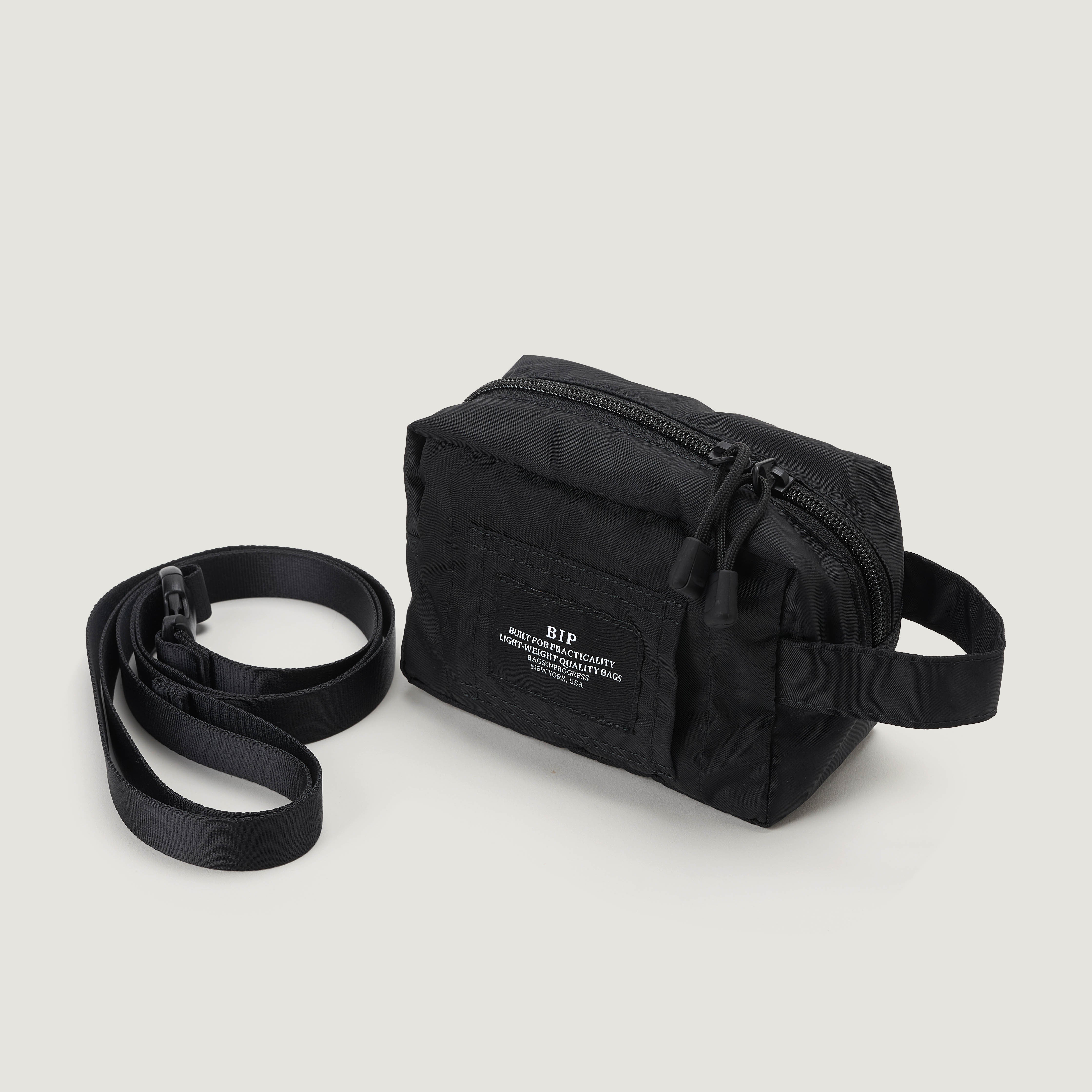 The Belt Pouch Mini by Bags in Progress is a small black rectangular crossbody bag with a front zipper pocket, adjustable strap, and a front label with white text.