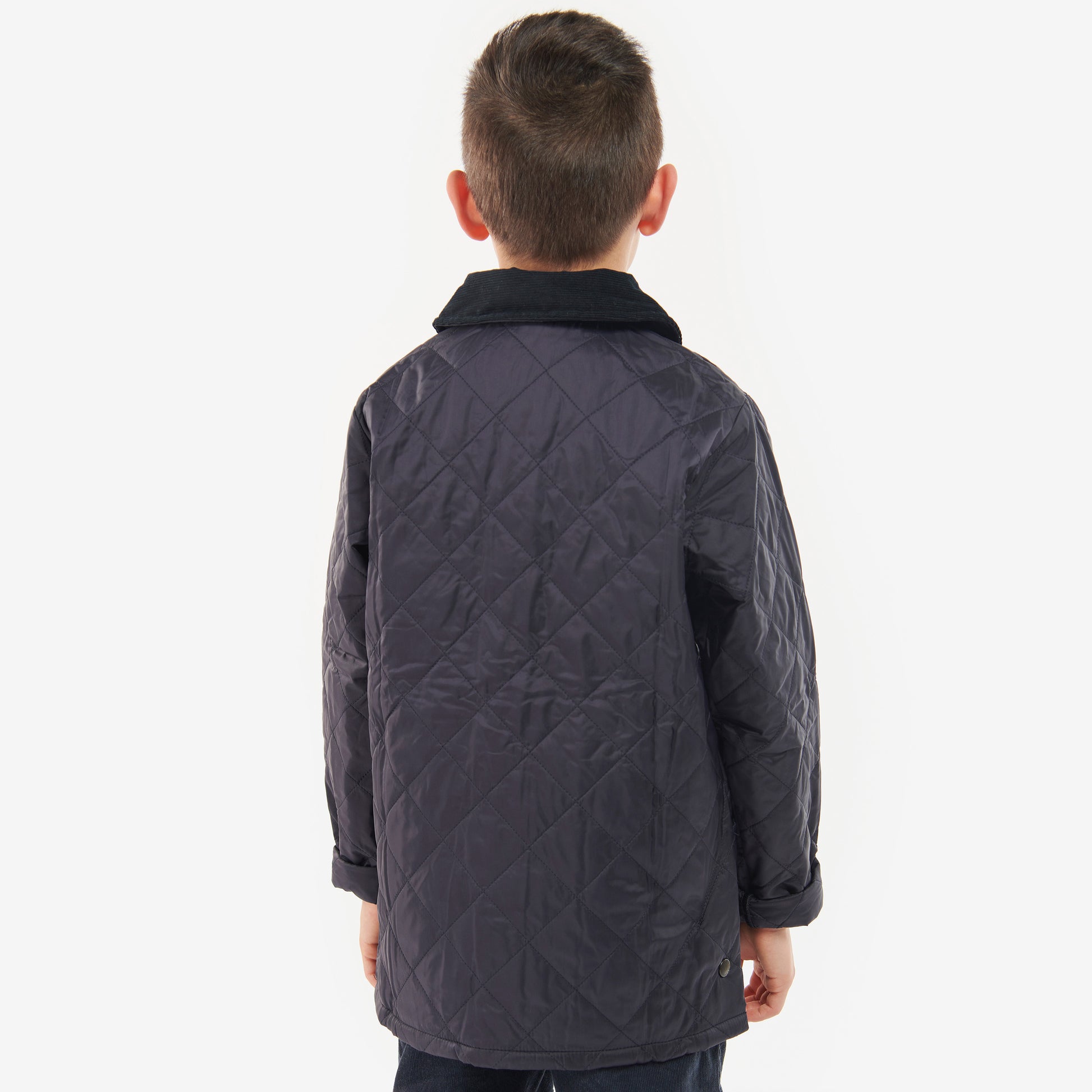 A young boy with short hair faces away, showcasing the Barbour Boys Liddesdale Quilted Jacket, featuring a dark quilted design and a neat needlecord collar against a light background.