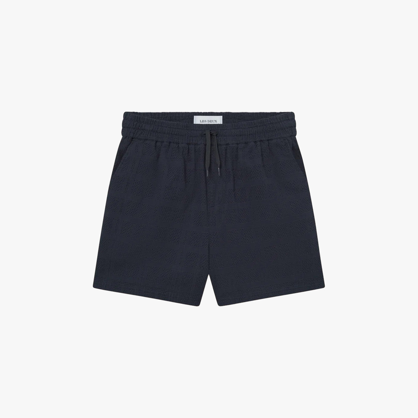 The Les Deux Charlie Shorts in navy blue cotton feature a drawstring and elastic waistband, side pockets, and a subtle textured pattern for effortless casual style, shown on a plain white background.