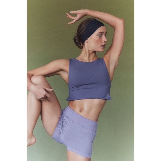 A woman in Free People Movement's activewear essentials striking a dance pose against a green background while wearing the Be Right Back Cami in Purple.