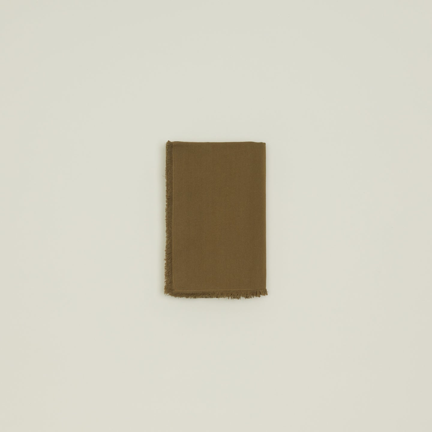 The Essential Cotton Tablecloth in olive by Hawkins New York is displayed folded with a fringed edge on a plain light background.