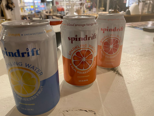 Three cans of Lemon Sparkling Water - Spindrift, Blood Orange Sparkling Water - Spindrift, and Grapefruit Sparkling Water - Spindrift, displayed on a wooden table in a store.