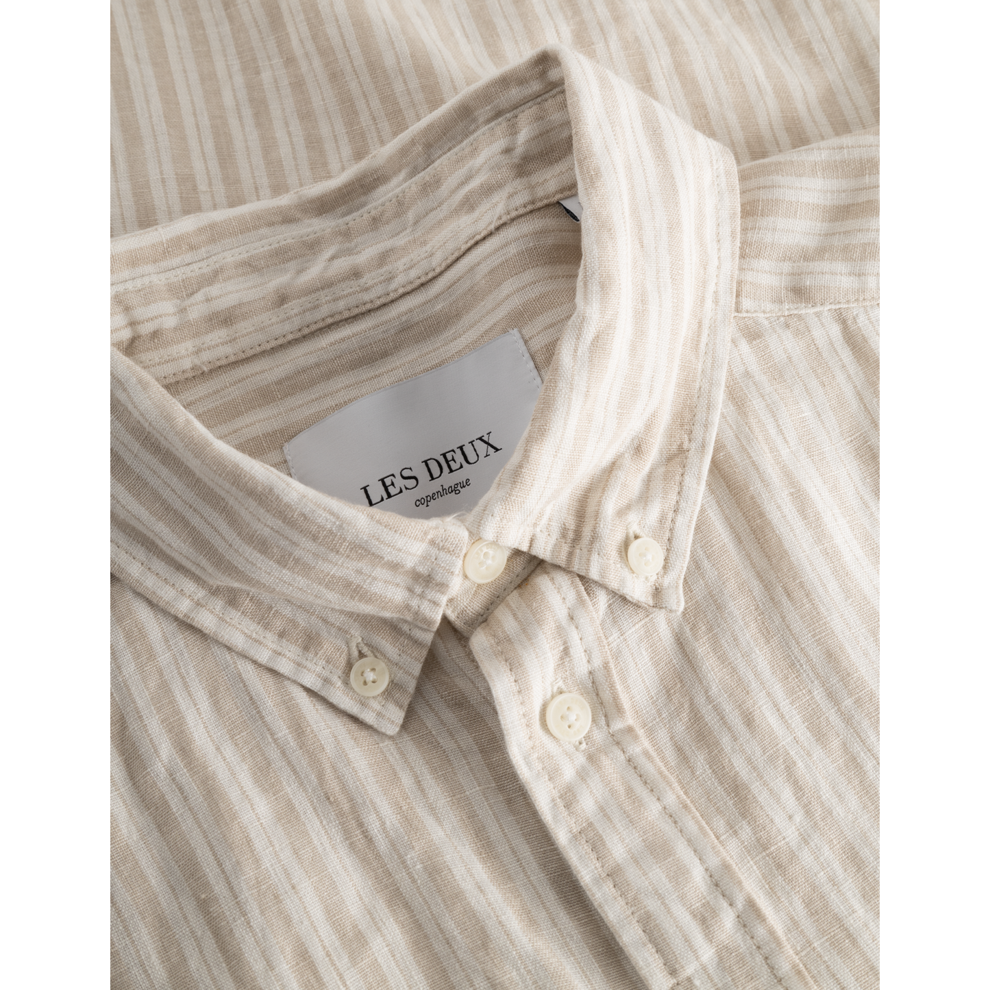 Close-up of a Kris Linen SS Shirt in Light Desert Sand/Light Ivory with a button-down collar showing the brand label "Les Deux".