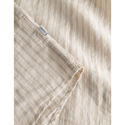 Close-up of a beige striped 100% linen fabric with a visible clothing tag reading "Les Deux Kris Linen SS Shirt, Light Desert Sand/Light Ivory".