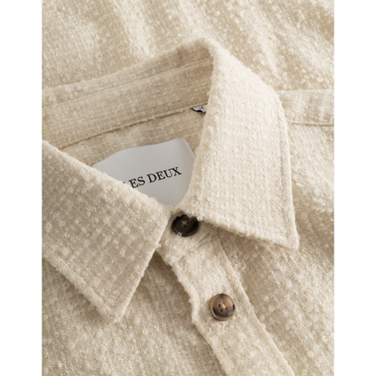 Close-up of a beige linen Kevin Boucle Shirt collar with a visible Les Deux tag that reads "es deux" and two brown buttons, crafted from recycled fibers.
