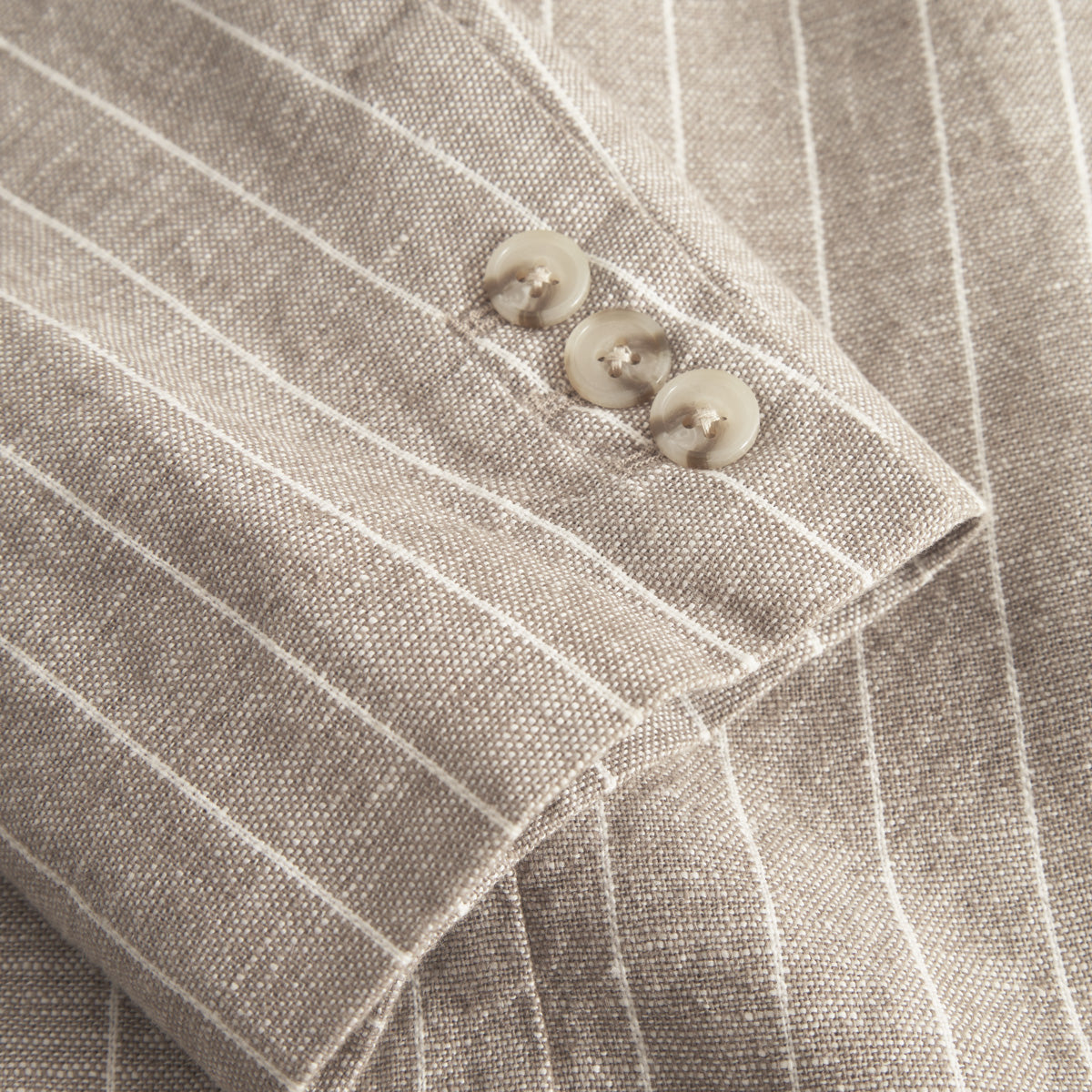 Close-up of the James Linen Blazer by Les Deux, featuring a beige pinstripe sleeve with three light buttons—ideal for stylish warm weather suiting.
