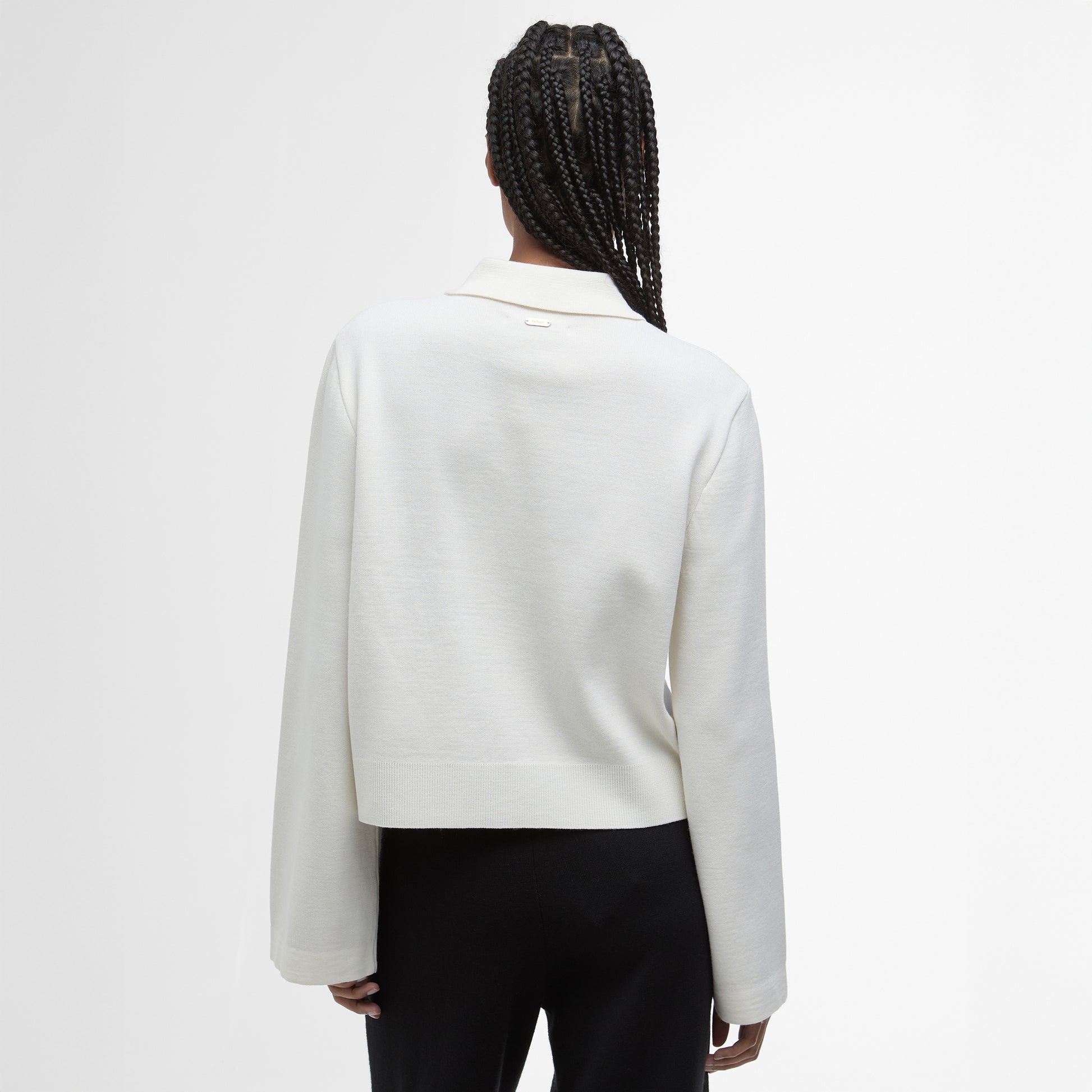 Person with braided hair wears a white Barbour Alma Knitted Zip Through Cardigan, made from a cotton-wool blend, and black pants, shown from the back against a plain white background.