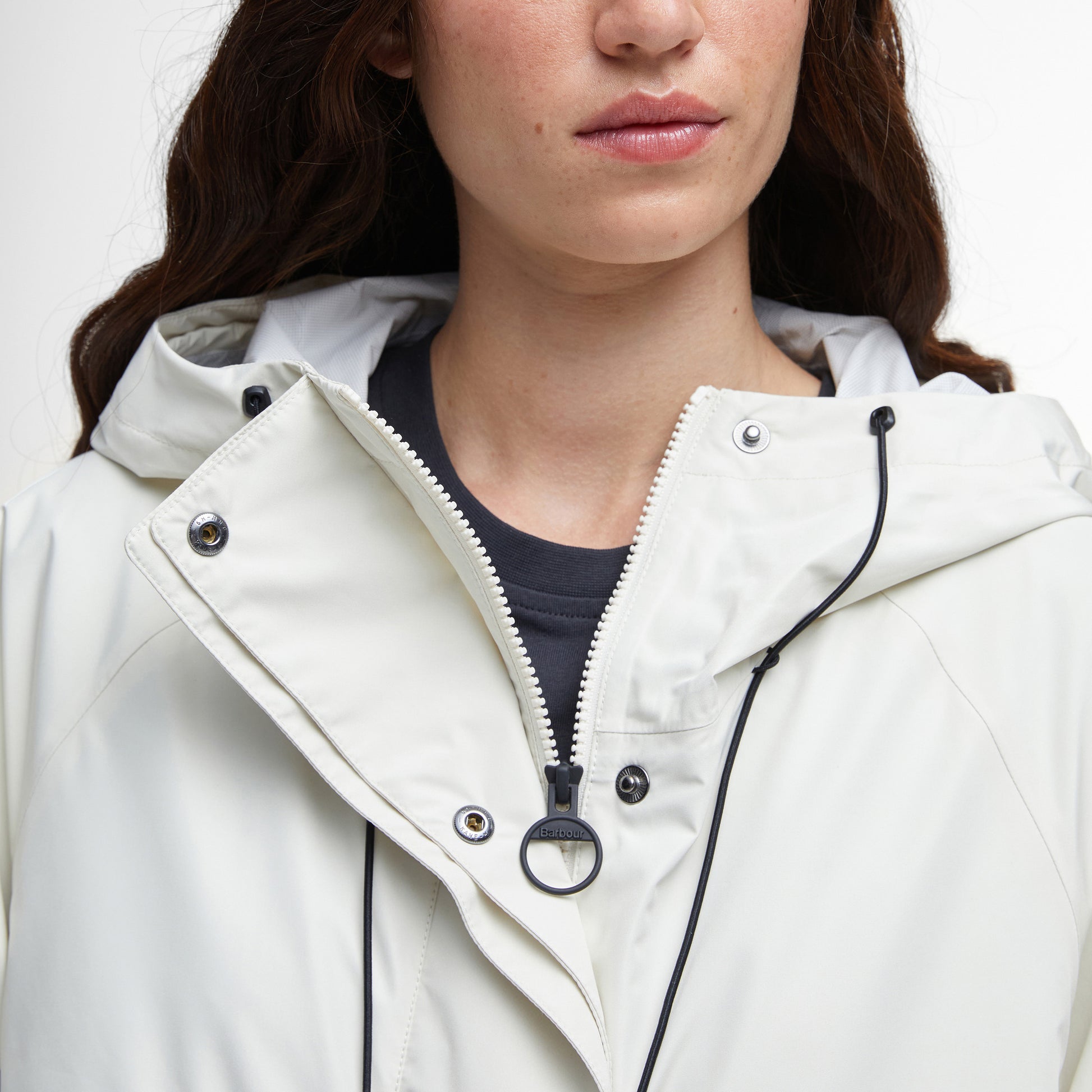 A woman models the Barbour Jayla Waterproof Parka in white with black drawstrings, partially zipped over a dark shirt—ideal for outdoor adventures.