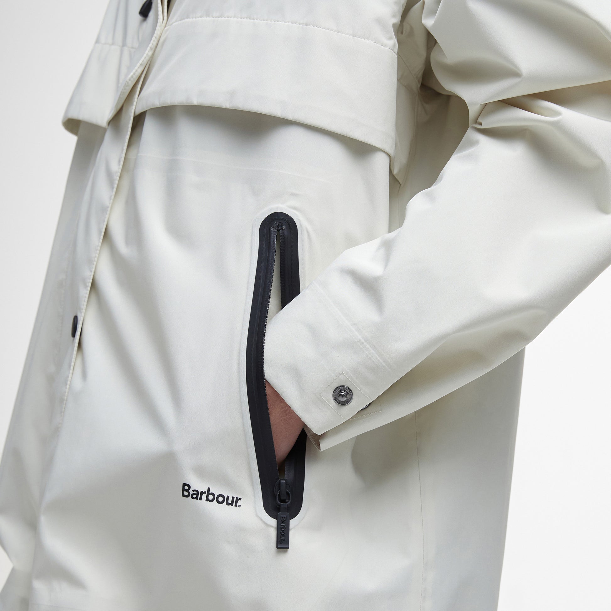 Someone wearing the Barbour Jayla Waterproof Parka with a hand in the zippered pocket, highlighting the Barbour logo and parka details.