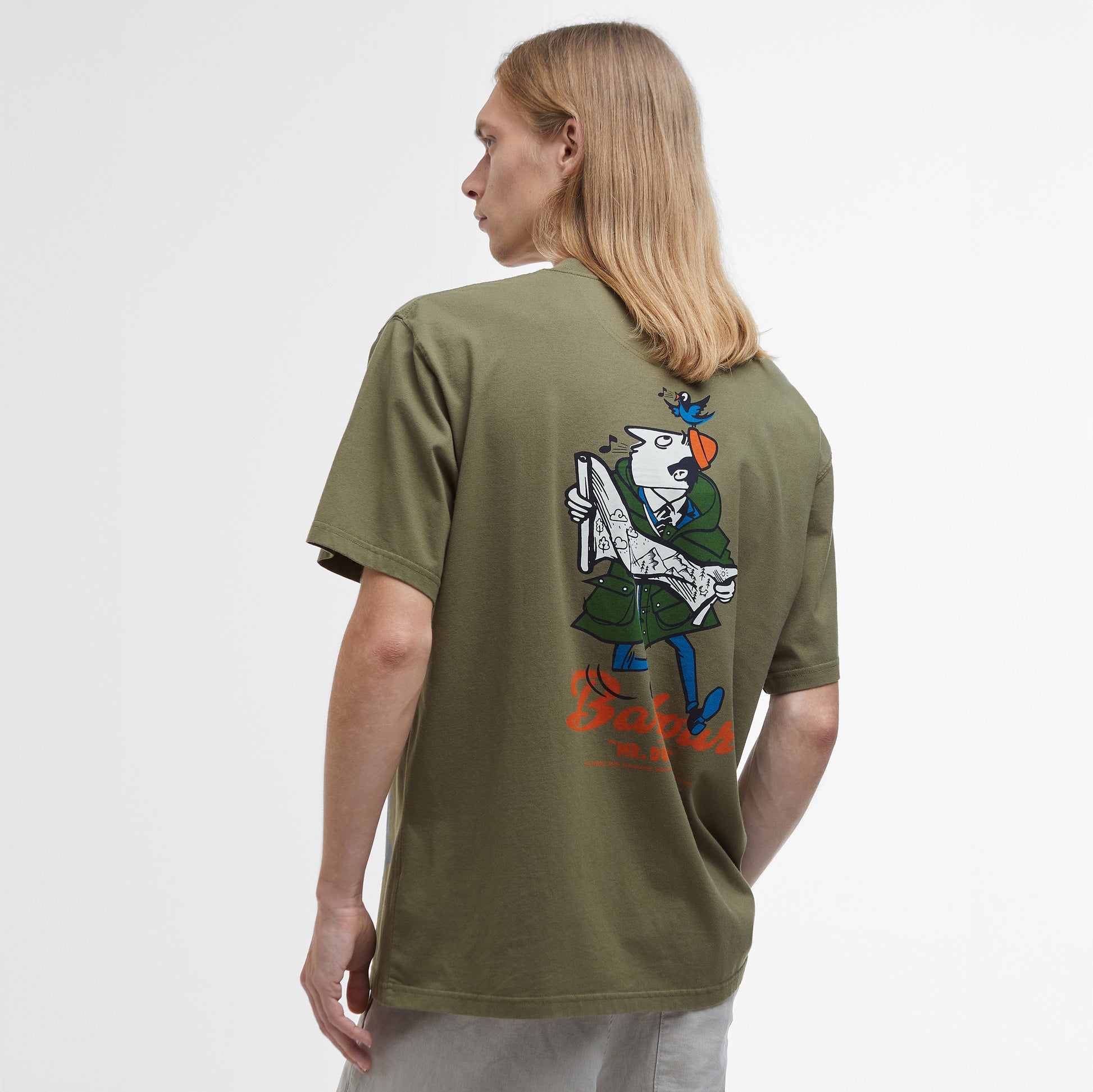 A person with long hair is shown from the back wearing the Barbour Regence Graphic T-Shirt in olive green, featuring an archive-inspired design of a royal character holding a book, posed neutrally.