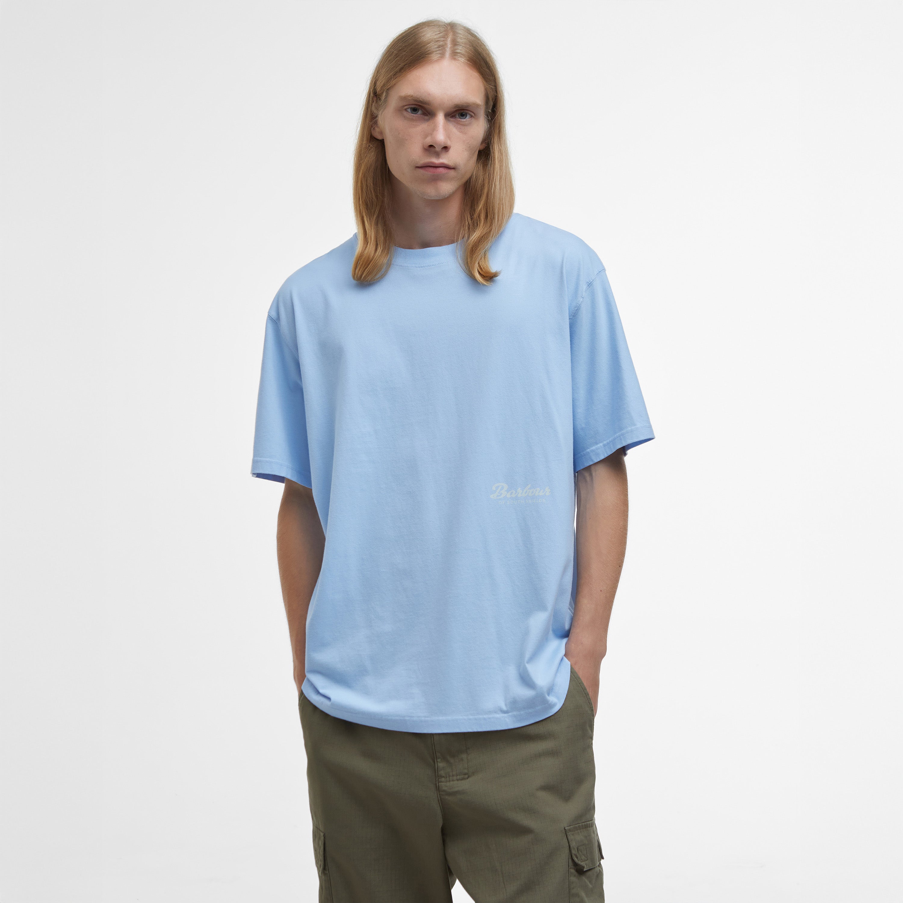 A person with long hair, wearing a Barbour Newclyde Graphic T-Shirt and green cargo pants, stands against a plain white background.