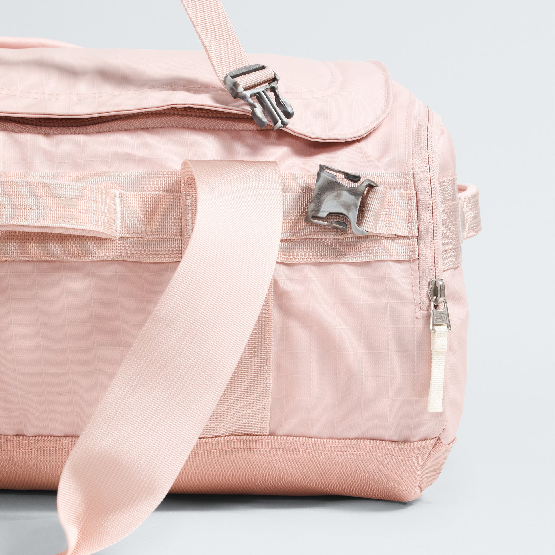 A close-up of The North Face Base Camp Voyager Duffel - 42L in light pink shows its lightweight design, strap, zipper, and metal buckle—your perfect travel companion.