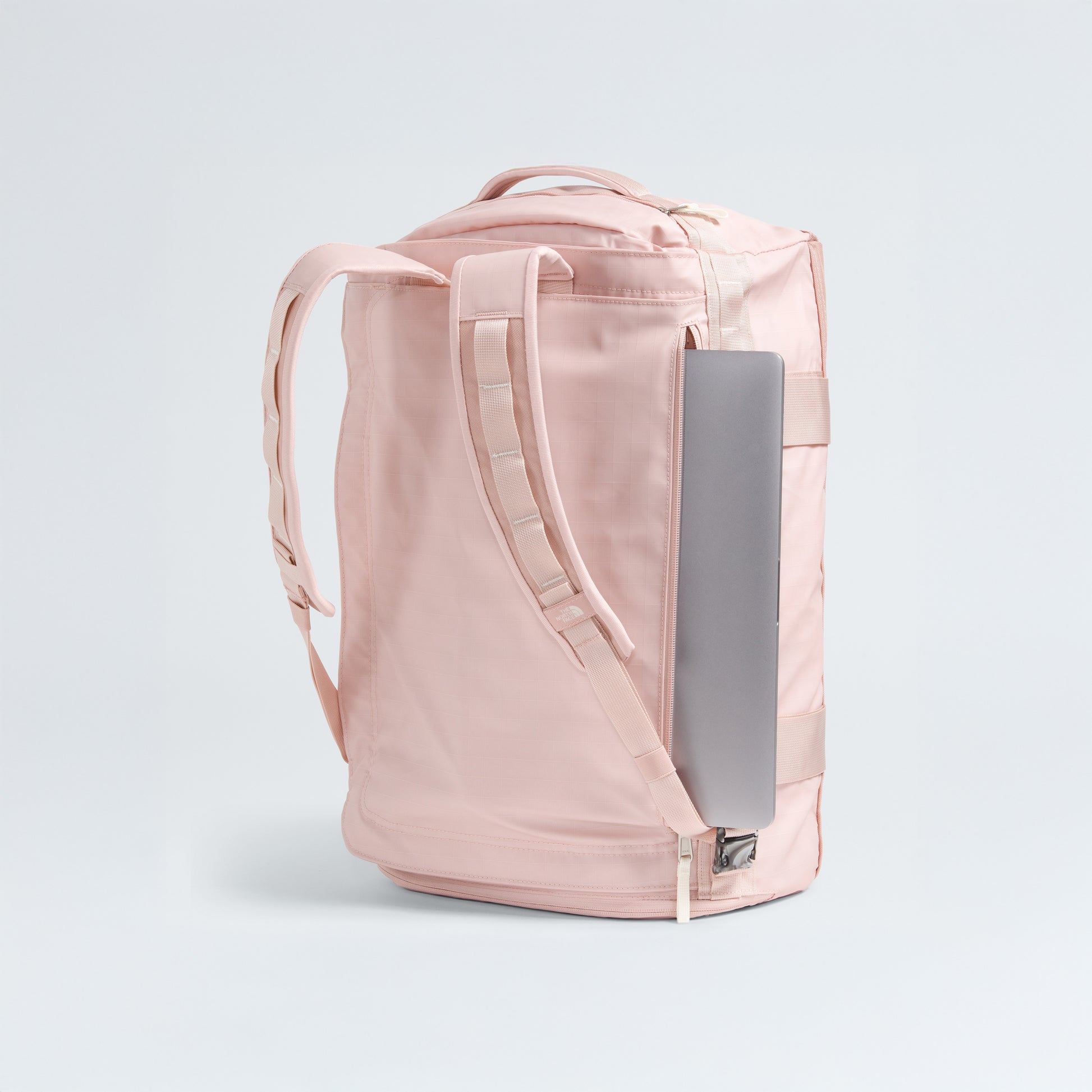 The North Face Base Camp Voyager Duffel - 42L stands upright, displaying its lightweight build and padded straps. A silver laptop is partly tucked into a side pocket. The plain, light background highlights this ideal travel companion.