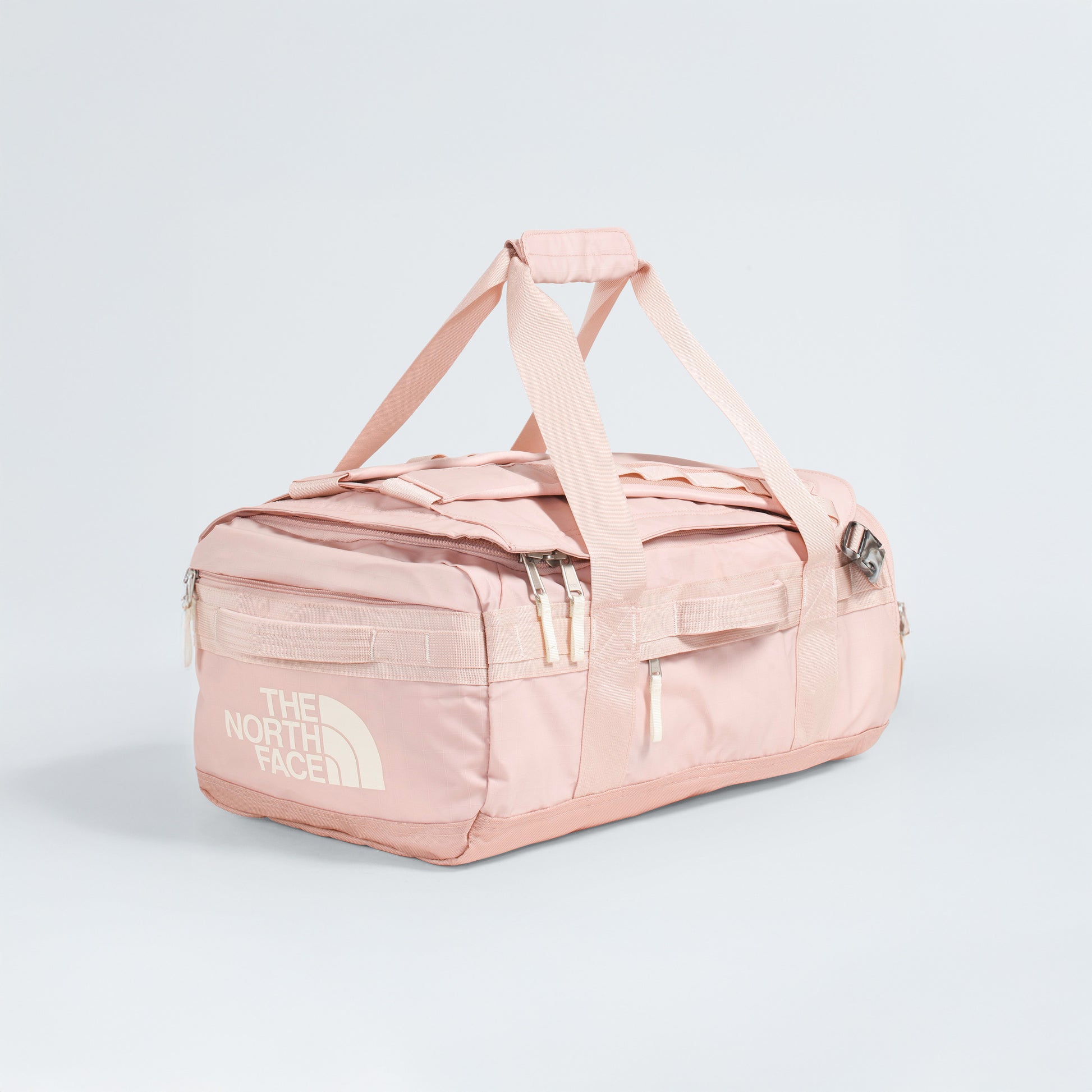 The North Face Base Camp Voyager Duffel - 42L in light pink features white zippers, handles, and logo. Shown on a plain light background, this lightweight bag is ideal for travel and adventure.