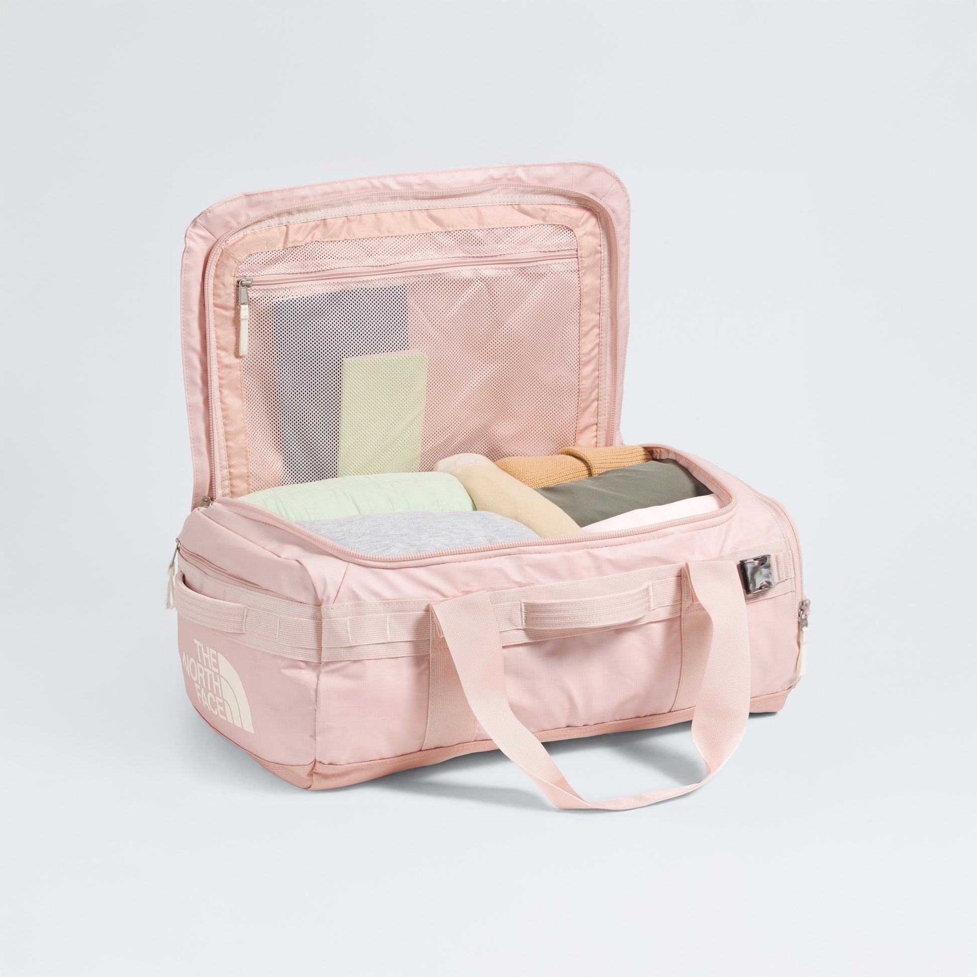 The North Face Base Camp Voyager Duffel - 42L in light pink with beige handles is open, showing rolled clothes and two mesh lid compartments—its lightweight design makes it the perfect travel companion.