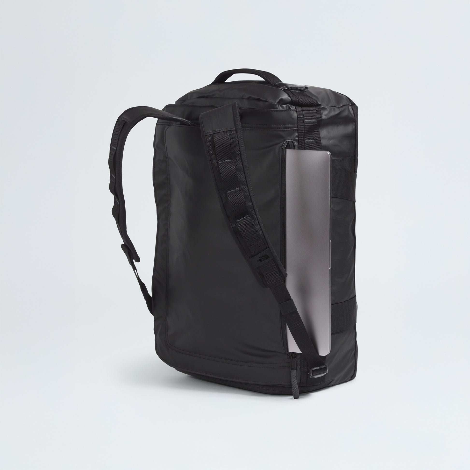 The North Face Base Camp Voyager Duffel - 42L in black features a side zipper pocket and holds a silver laptop partially inserted, highlighting its lightweight, travel-ready design, shown against a plain light background.