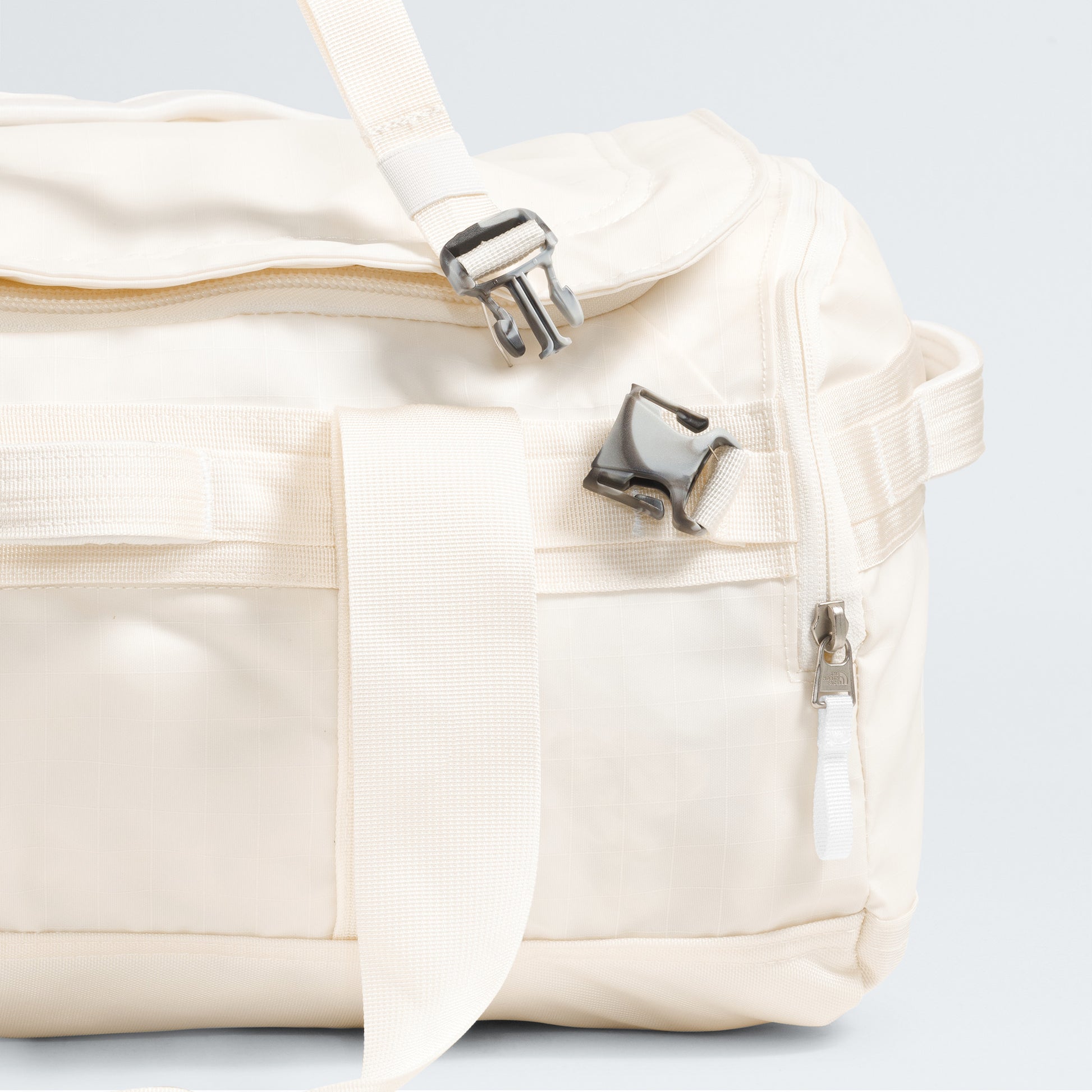 A close-up of The North Face Base Camp Voyager Duffel - 42L, a cream travel bag with zippers, a buckle, and a carrying handle shown against a plain background.