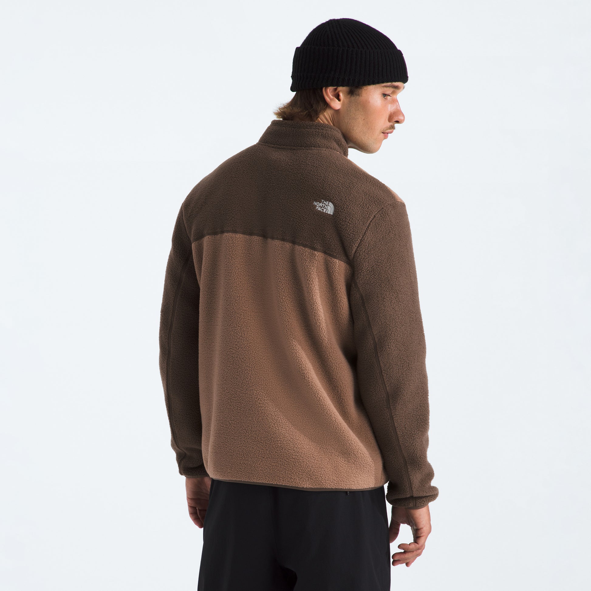 Someone wearing The North Face M Yumiori 1/4 Zip fleece jacket in brown and tan with a black knit beanie, seen from behind against a plain background.