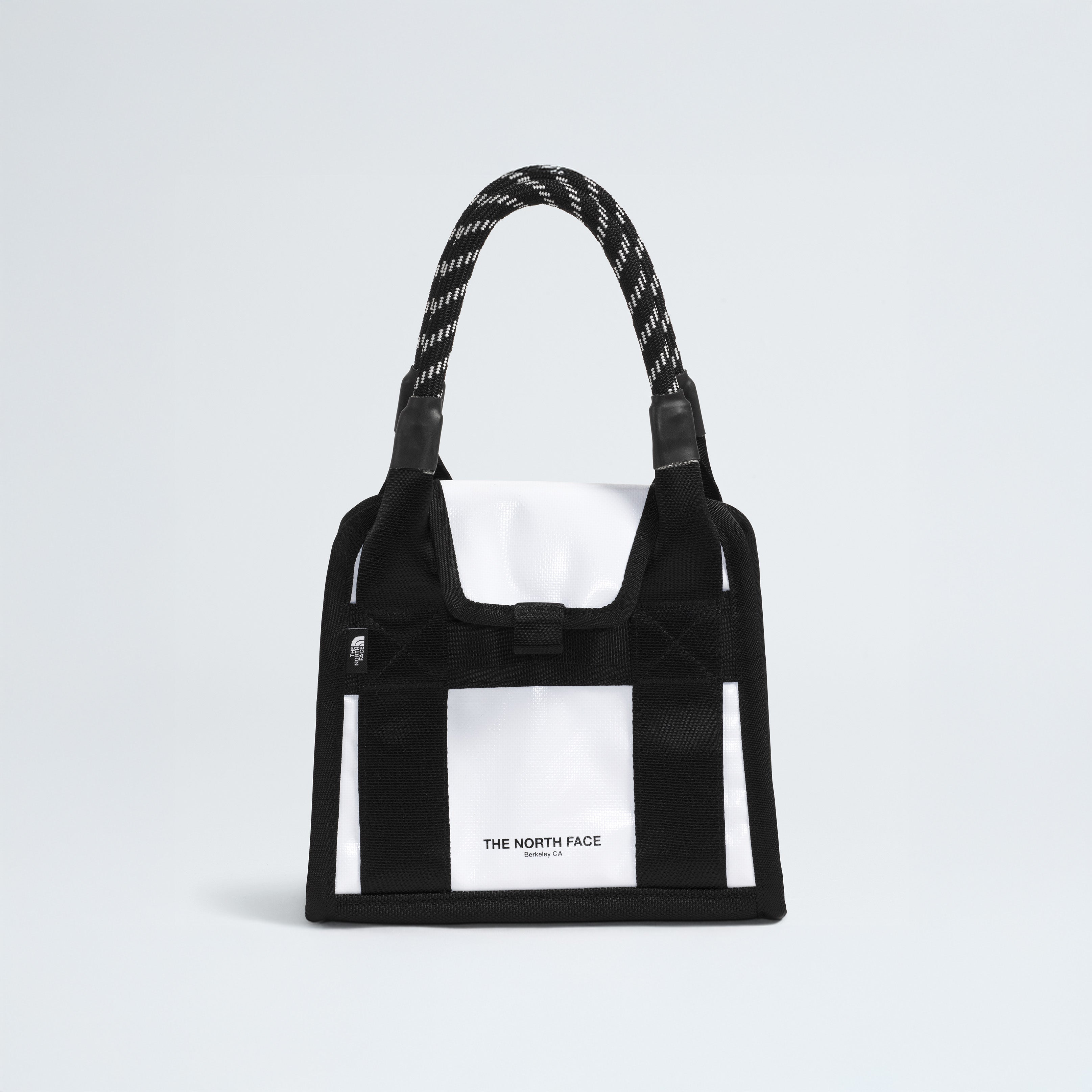 A black and white Base Camp Mini Tote features a patterned handle and "The North Face" logo on the front, crafted from recycled fabric for sustainability.