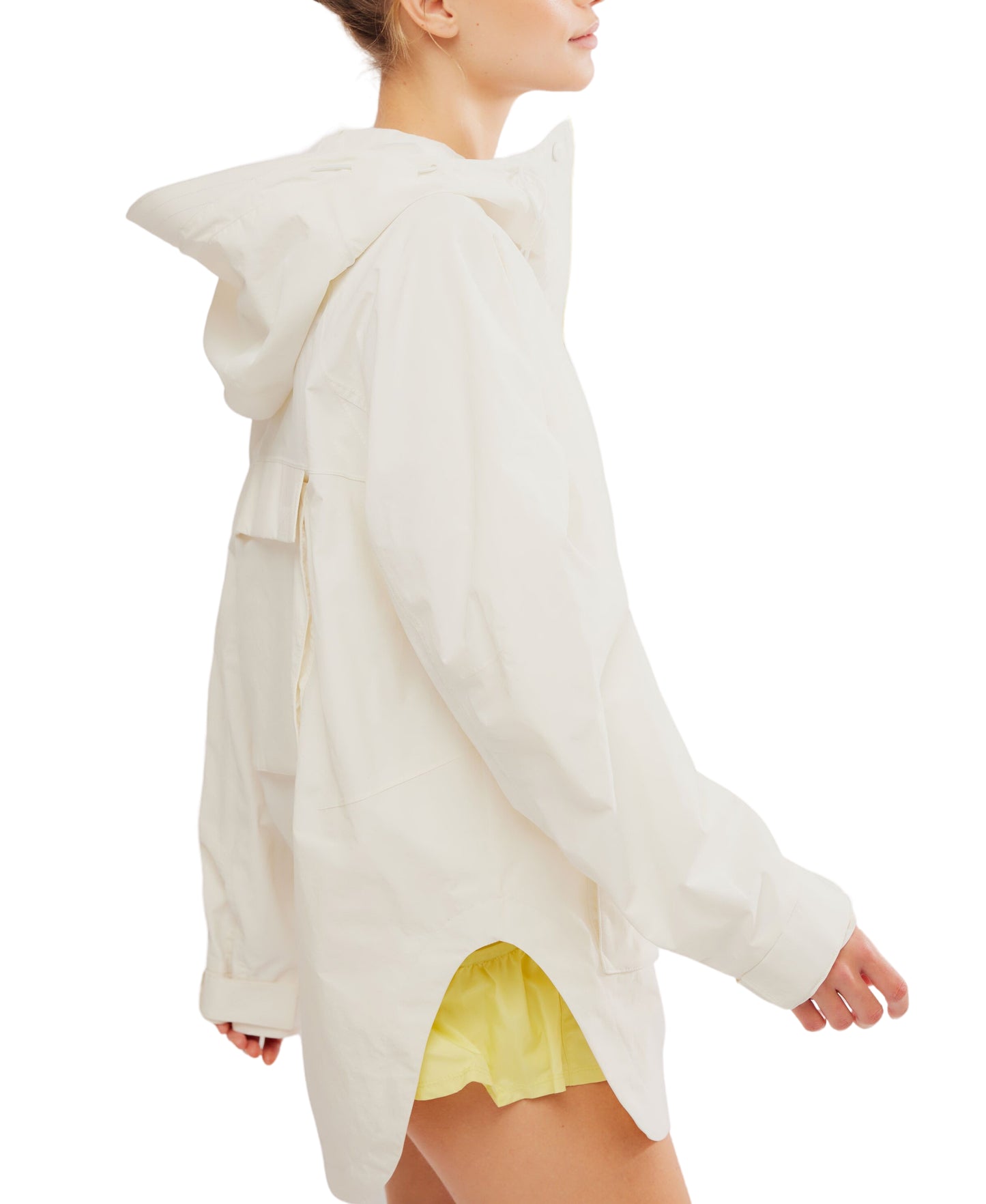 Woman seen from the side, wearing an oversized white waterproof hooded Singin in the Rain Jacket with large pockets and yellow shorts by Free People Movement.