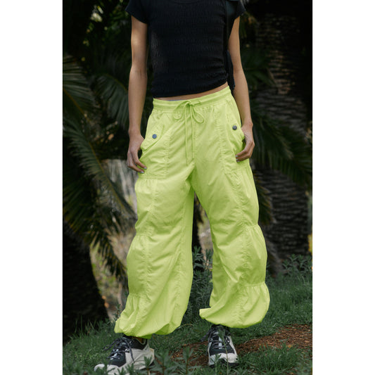 Person wearing Free People Movement's Set Me Free Pant in Lime and black sneakers standing in a garden.