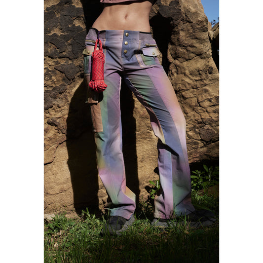 A person wearing Free People Movement's Printed Cascade Flare trousers in Galaxy Gradient and holding a coiled red rope stands against a rock background, focusing on the midsection.