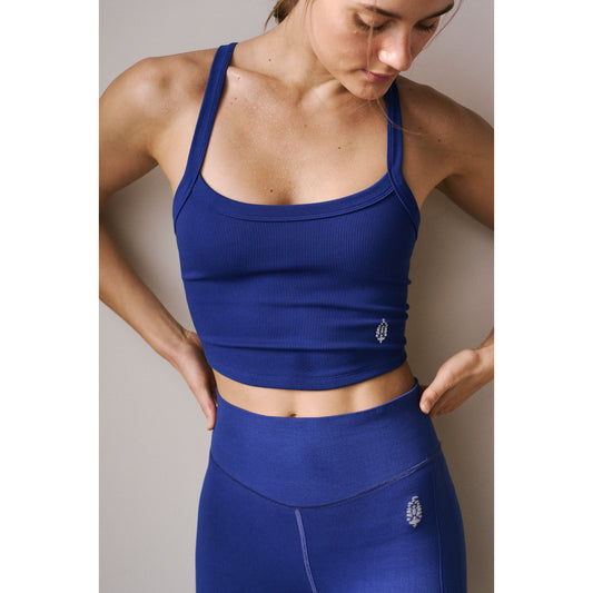 Woman in a Free People Movement All Clear Cami Solid sports bra and leggings in Saphire Skies, posing with her hand on her hip, looking downward against a neutral background.