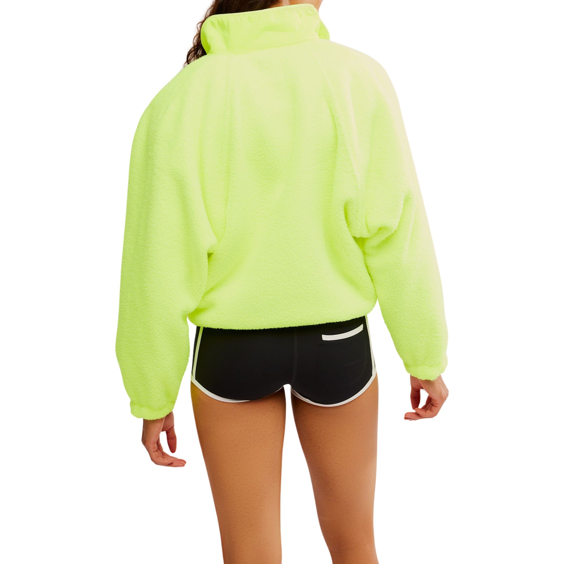 Woman from behind wearing a Free People Movement Hit The Slopes Jacket in Highlighter with zippered pockets and black athletic shorts with white trim.