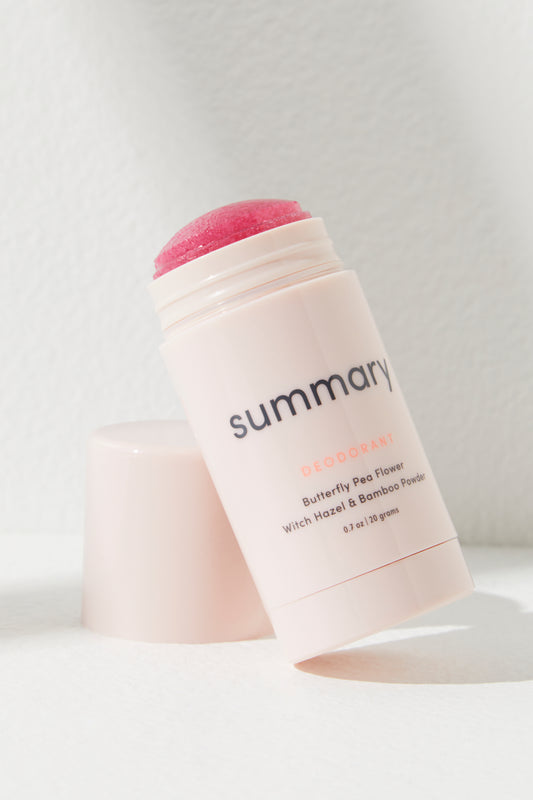 Pink Summary Deodorant stick labeled "Free People Movement" with cap off, leaning against a white wall in bright sunlight.